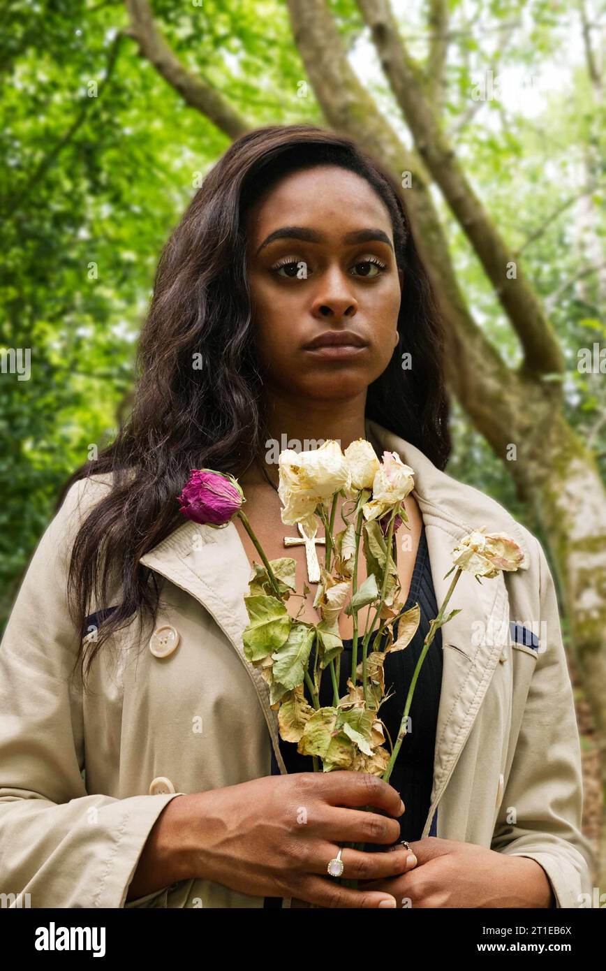 Junge schwarze Frau, die im Wald steht und Rosen hält Stockfoto