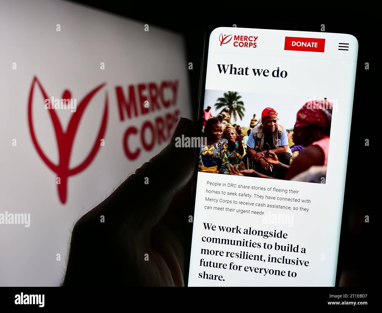 Person, die ein Handy hält, mit Webseite der humanitären Hilfsorganisation Mercy Corps vor dem Logo. Konzentrieren Sie sich auf die Mitte des Telefondisplays. Stockfoto