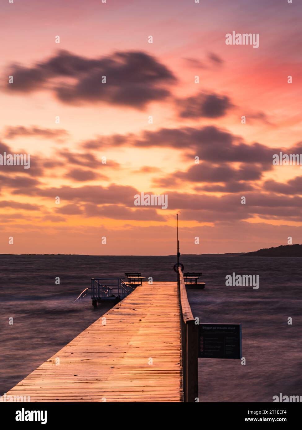 Ruhiger Sonnenuntergang über einem hölzernen Pier an einem windigen schwedischen Strand. Stockfoto