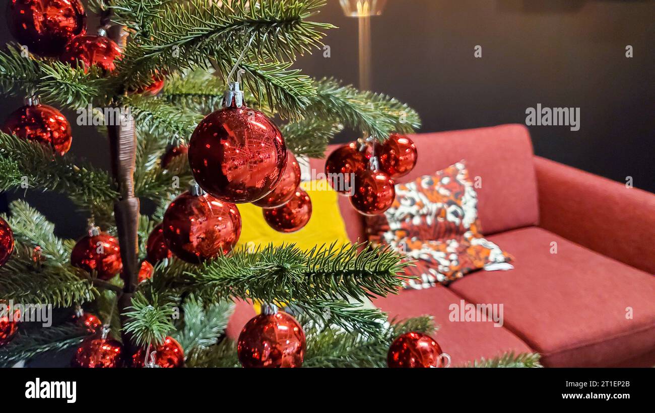 Weihnachtsbaum mit roter Dekoration im Wohnzimmer mit gemütlichem Sofa und Kissen Stockfoto