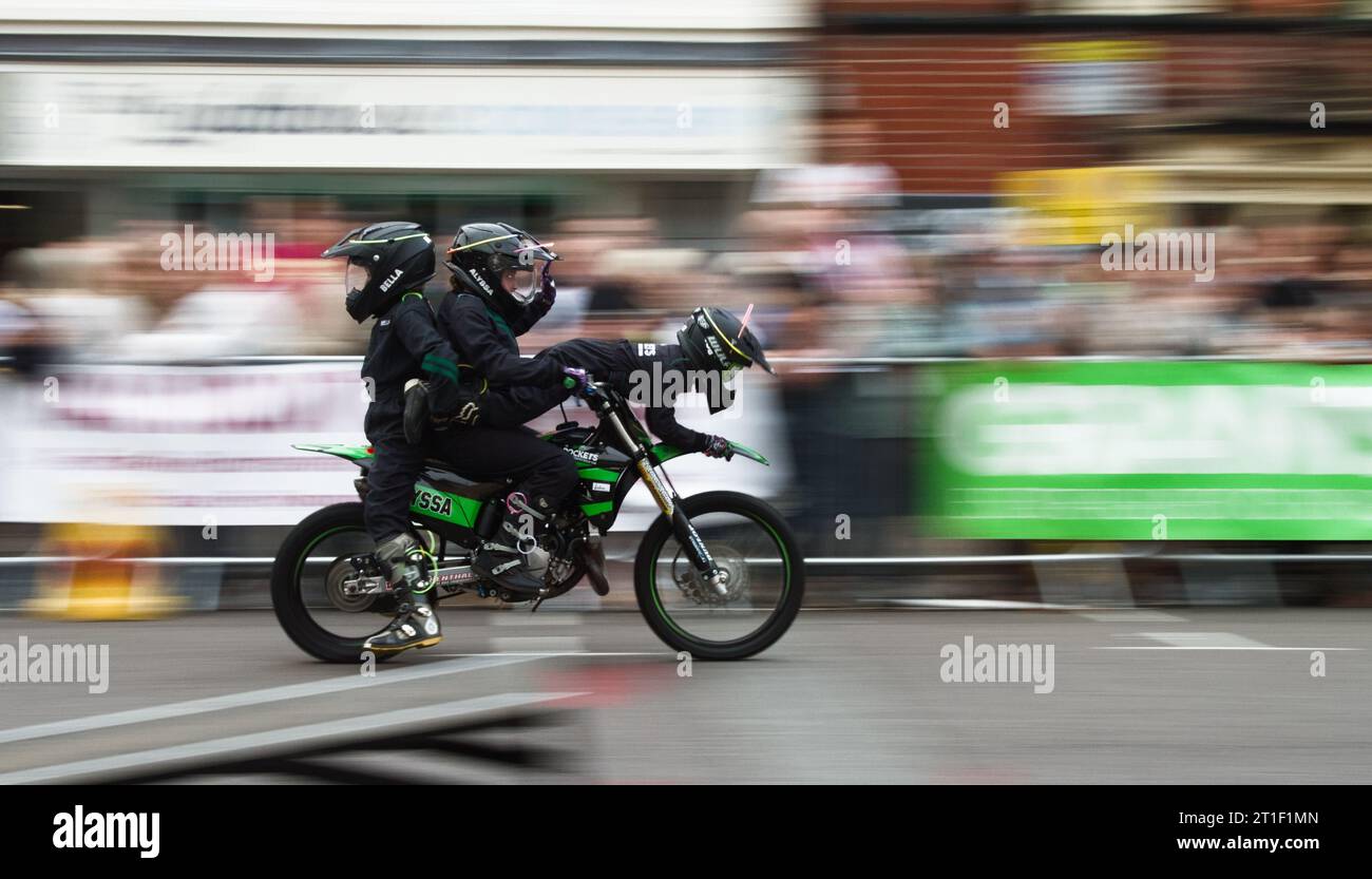 Drei Mitglieder des Rockets Childrens Motorbike Display Teams Balancing Together on One Bike with Motion Blur Show Speed, Ringwood Carnival, Großbritannien Stockfoto