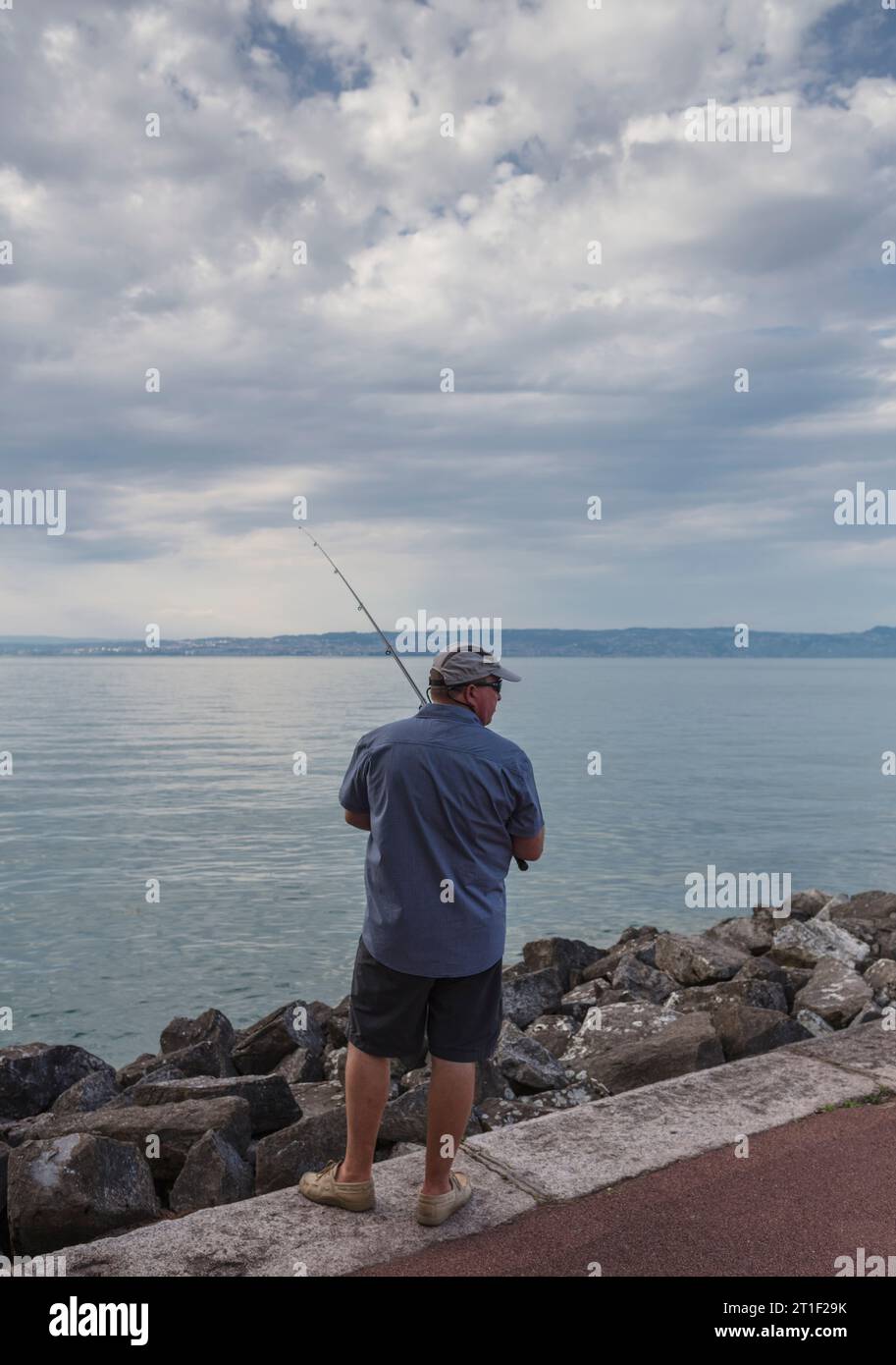 Evian-les-Bains, Frankreich. Ein Fischer am Seeufer, bei Sonnenuntergang. Evian-les-Bains ist eine Stadt im nördlichen Teil des Departements Haute-Savoie (R Stockfoto