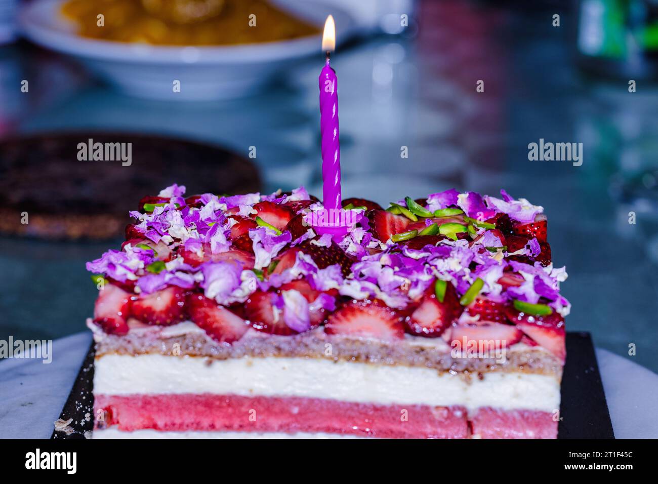 Ein köstlicher weißer Kuchen mit bunten Blumen und beleuchteten Kerzen, perfekt für einen besonderen Anlass Stockfoto