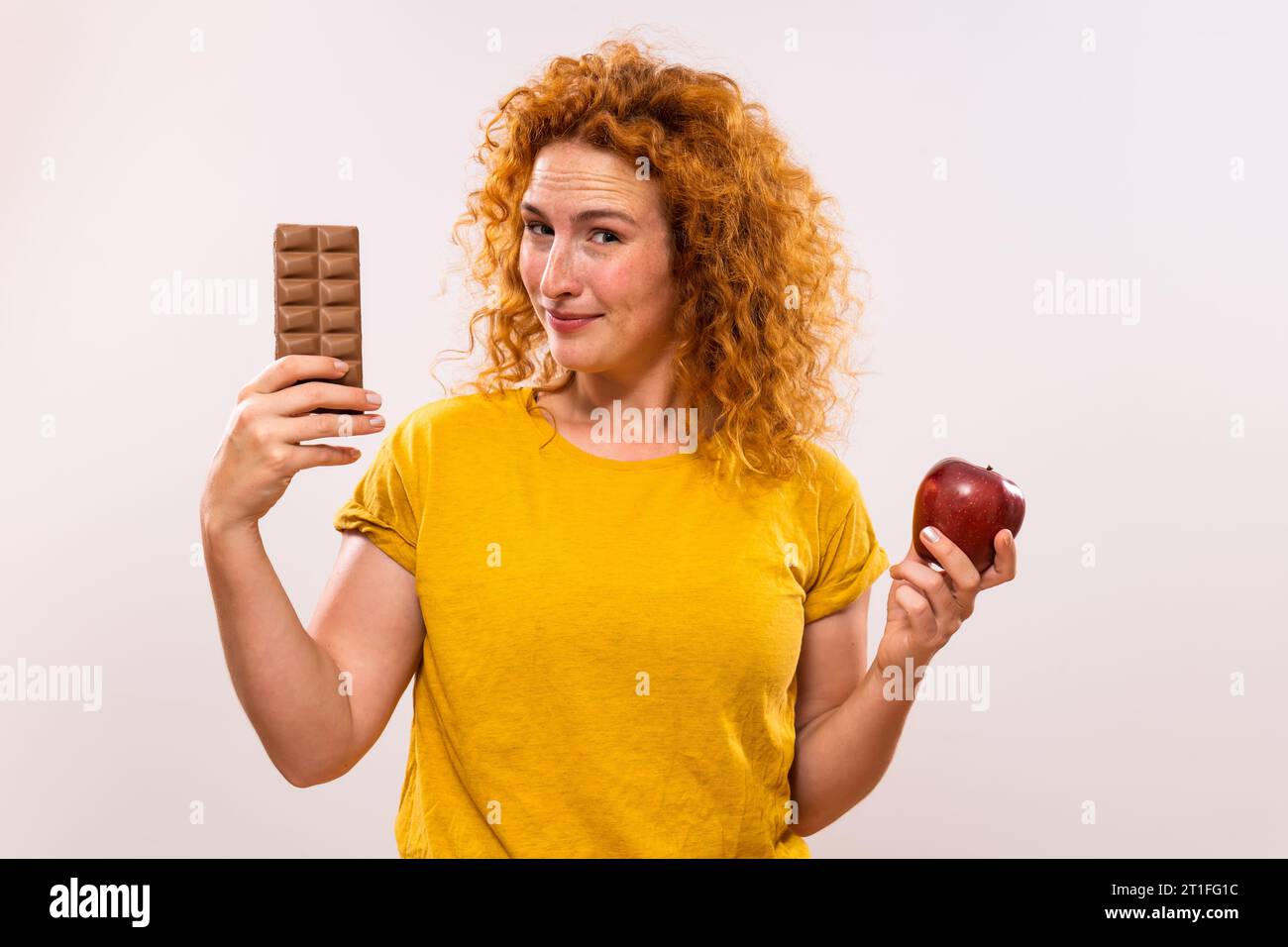 Niedliche Ingwerfrau, die Zweifel mit gesunder und ungesunder Ernährung hat. Stockfoto