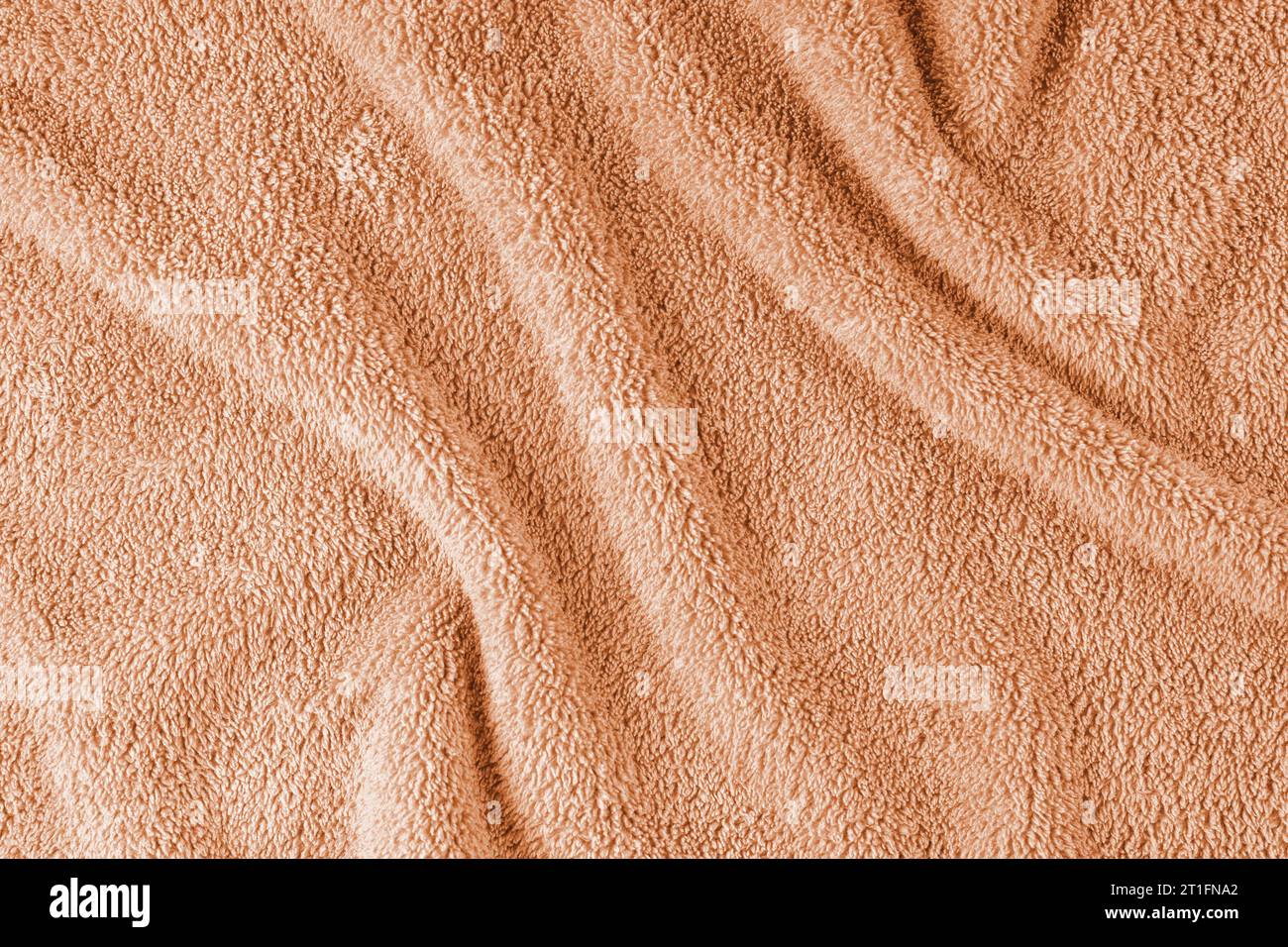 Frotteetuch, orangefarbener Hintergrund mit Handtuchbeschaffenheit. Zerknittertes und zerknittertes, weiches, flauschiges Textilbad oder Strandtuch. Draufsicht, Nahaufnahme. Stockfoto