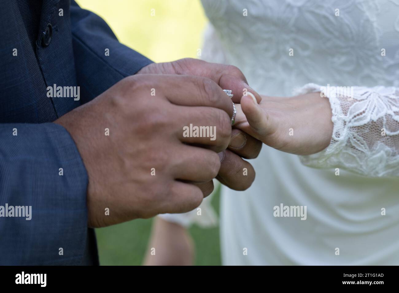 Masuline Hände des Bräutigams legen den Ehering an den Finger seiner Braut als Symbol seiner Verpflichtung. Stockfoto