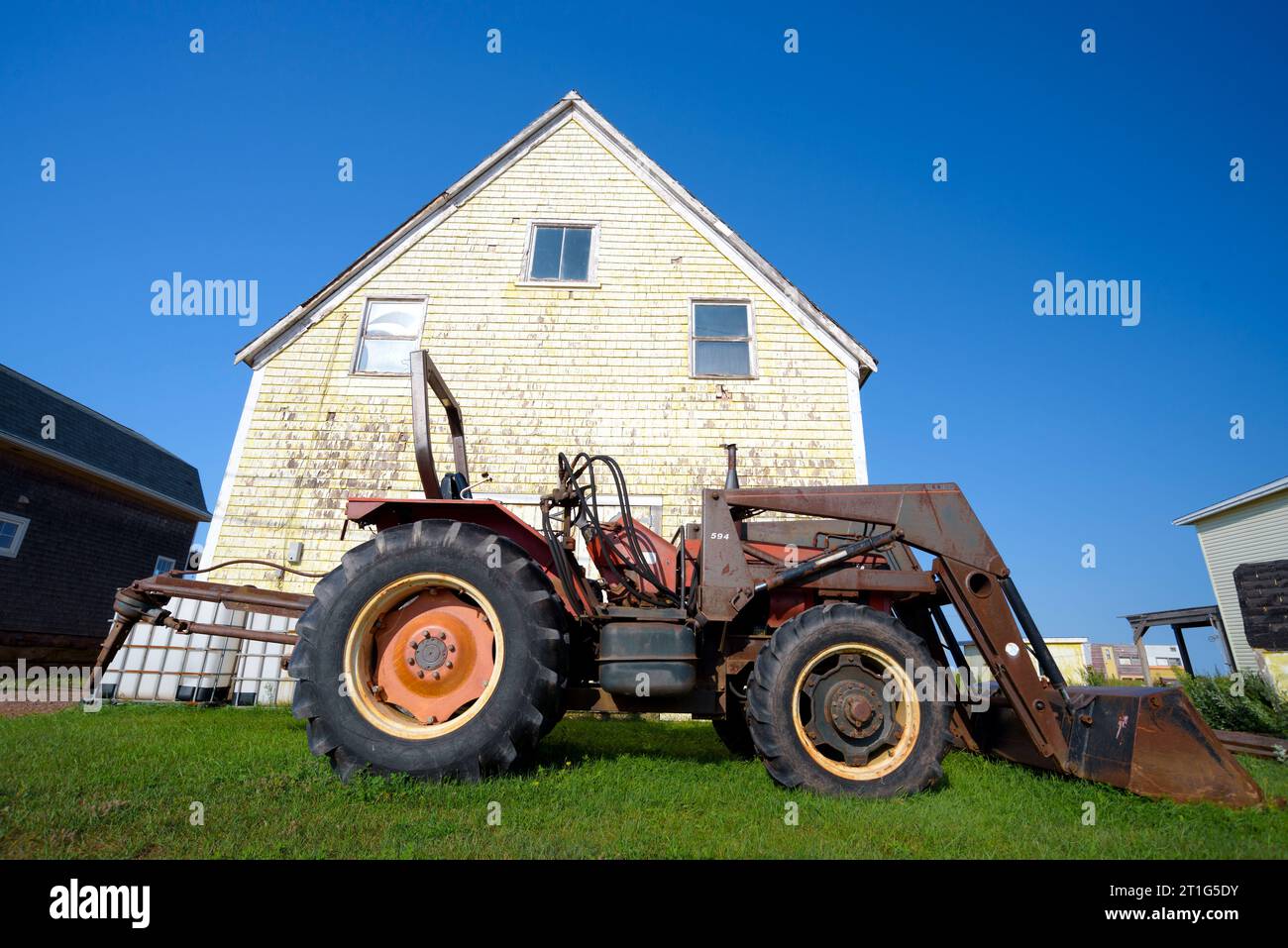 Ein alter rostiger Traktor, der auf dem Rasen eines verwitterten Hauses in North Rustico, Prince Edward Island, Kanada, geparkt wurde Stockfoto