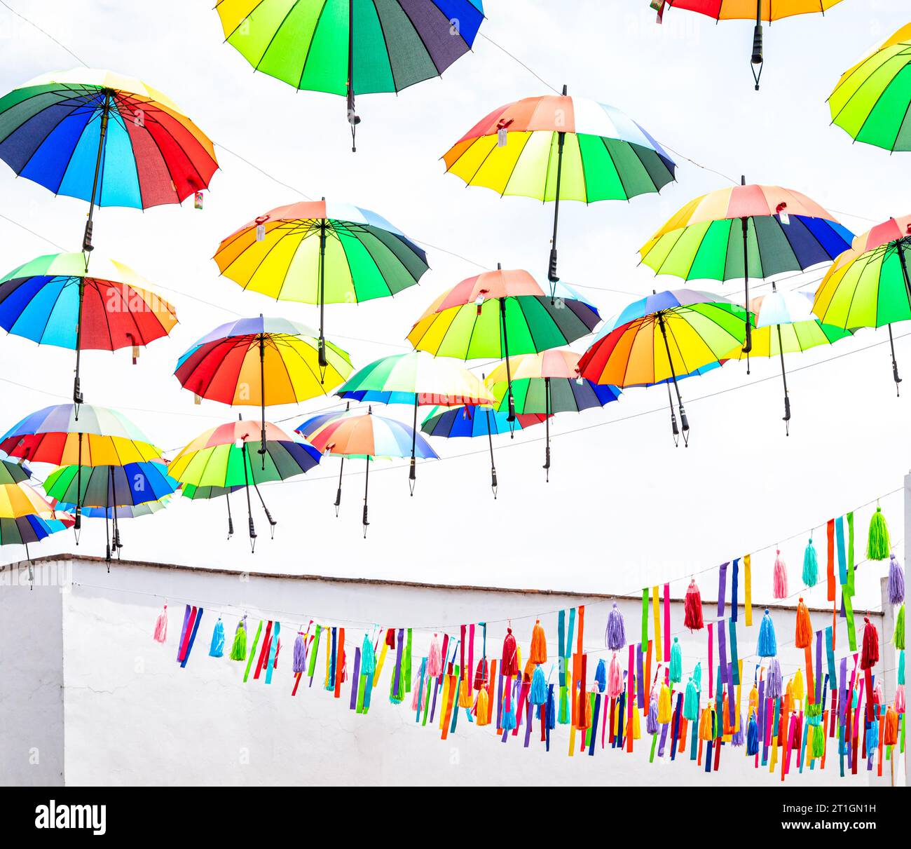 Bunte Regenschirme und Straßendekorationen vor einem weißen Himmel und Gebäude in Metepec, Mexiko. Stockfoto