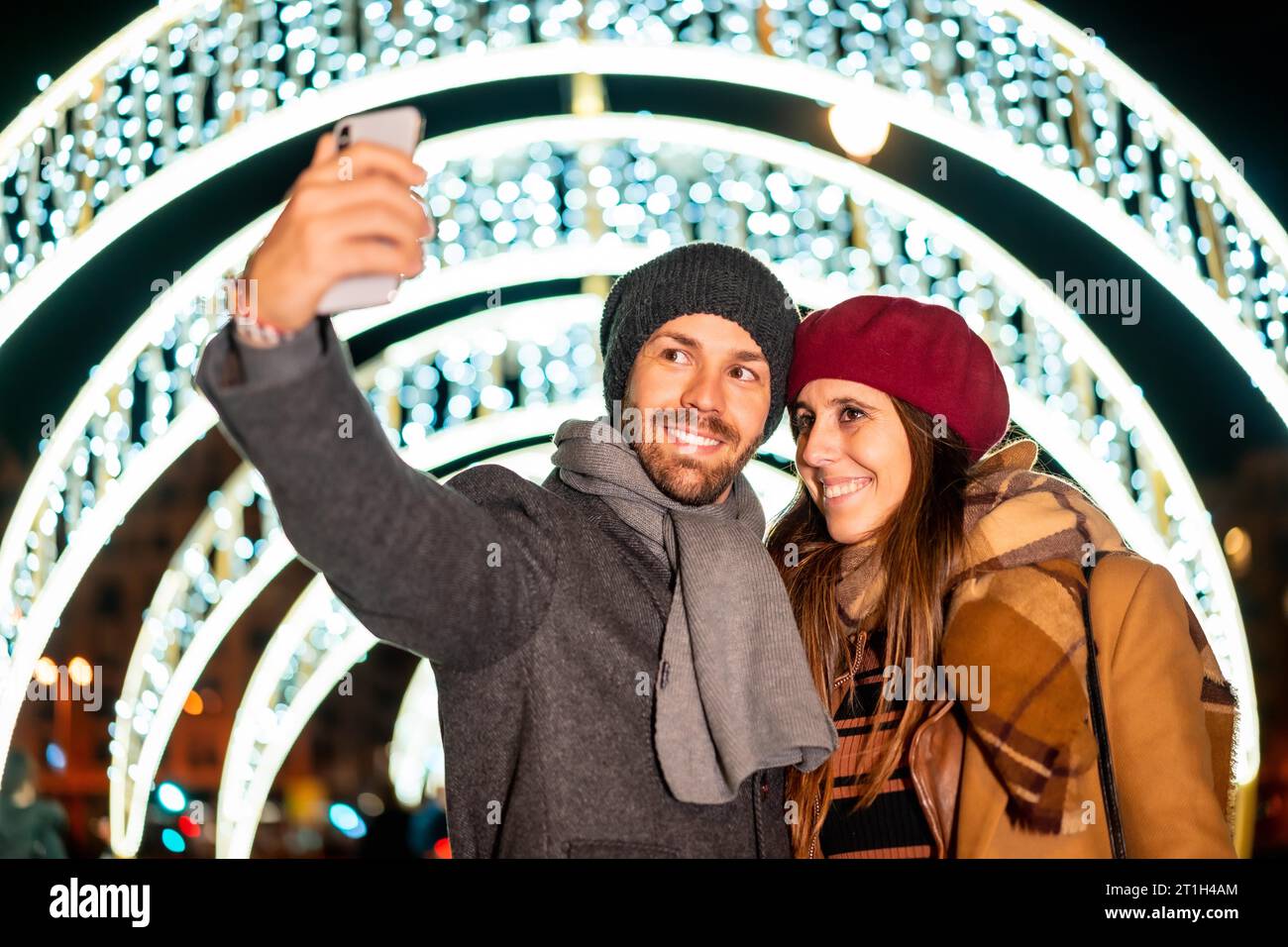 Winterporträt eines kaukasischen Paares, das die Weihnachtslichter der Stadt genießt und ein Selfie mit dem Handy für soziale Netzwerke und Lifestyle macht Stockfoto