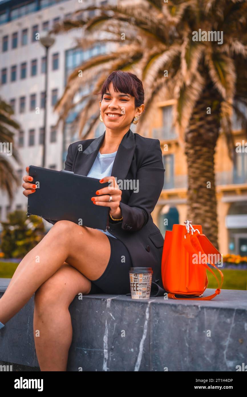 Unternehmersession, eine junge Geschäftsfrau in einem schwarzen Blazer und weißen Sneakers auf Pause von der Arbeit. Bereiten Sie das nächste Meeting mit einem Kaffee und vor Stockfoto