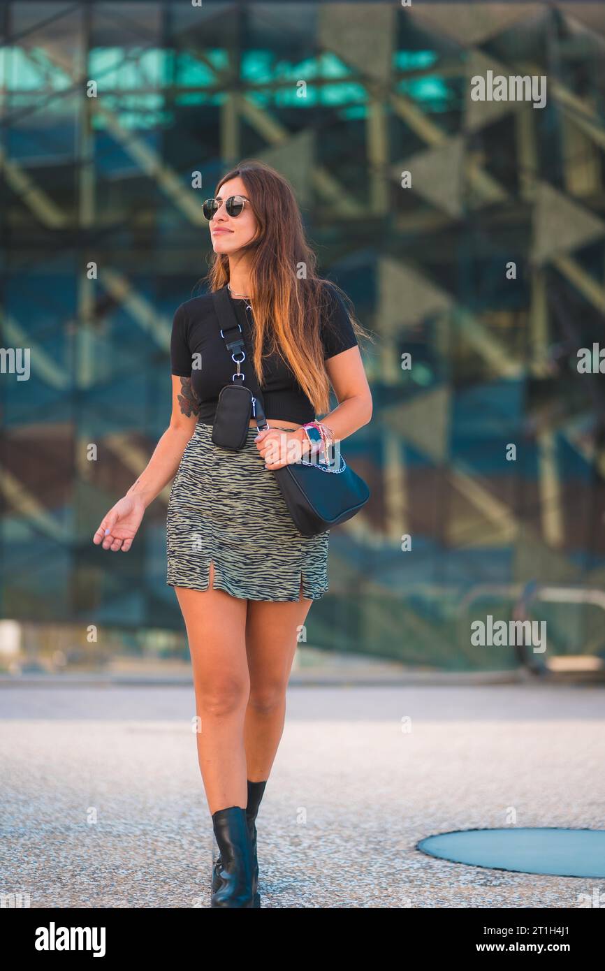 Lebensstil einer jungen kaukasischen Brünetten Geschäftsfrau vor dem Bürogebäude zu Fuß. Mit grünem Rock und Sonnenbrille Stockfoto