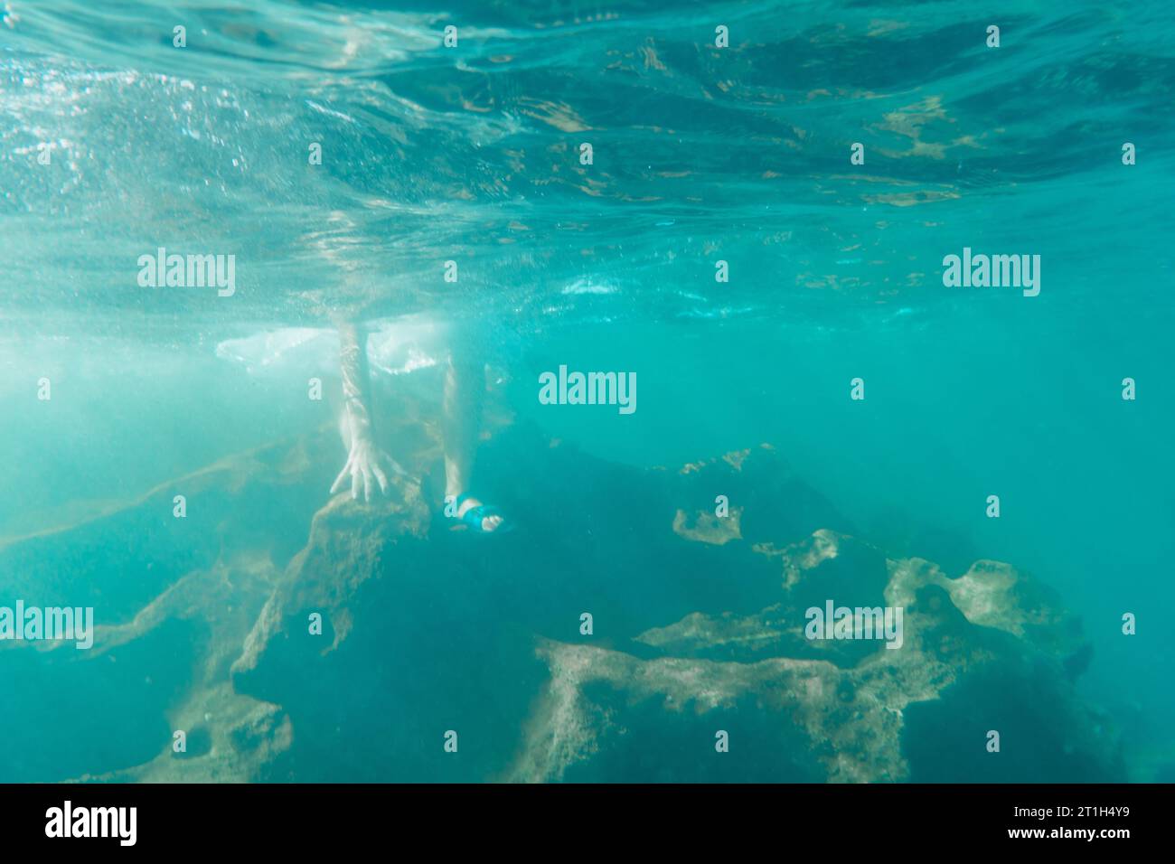 Eine junge kaukasische Brünette mit Flip Flops, die ins Wasser kommen, Unterwasserbild, Sommerleben Stockfoto
