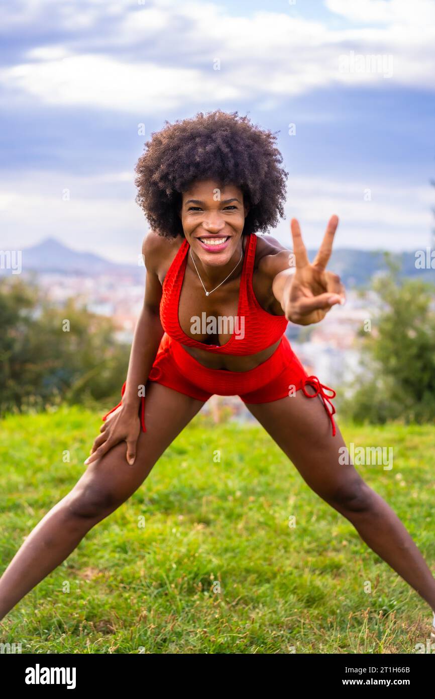 Fitness mit einem jungen schwarzen Mädchen mit Afro-Haar, Übung Nummer zwei, Training auf dem Feld, roter Sportanzug, fittes Mädchen, gesundes Leben, Kopie Stockfoto