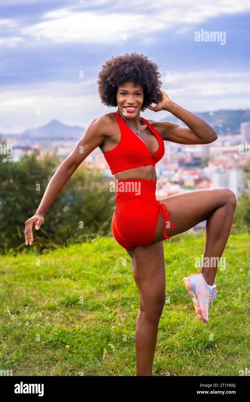 Fitness mit einem jungen schwarzen Mädchen mit Afro-Haaren, Dehnen, Training auf dem Feld, roter Sportanzug, fittes Mädchen, gesundes Leben, Kopierpaste Raum Stockfoto