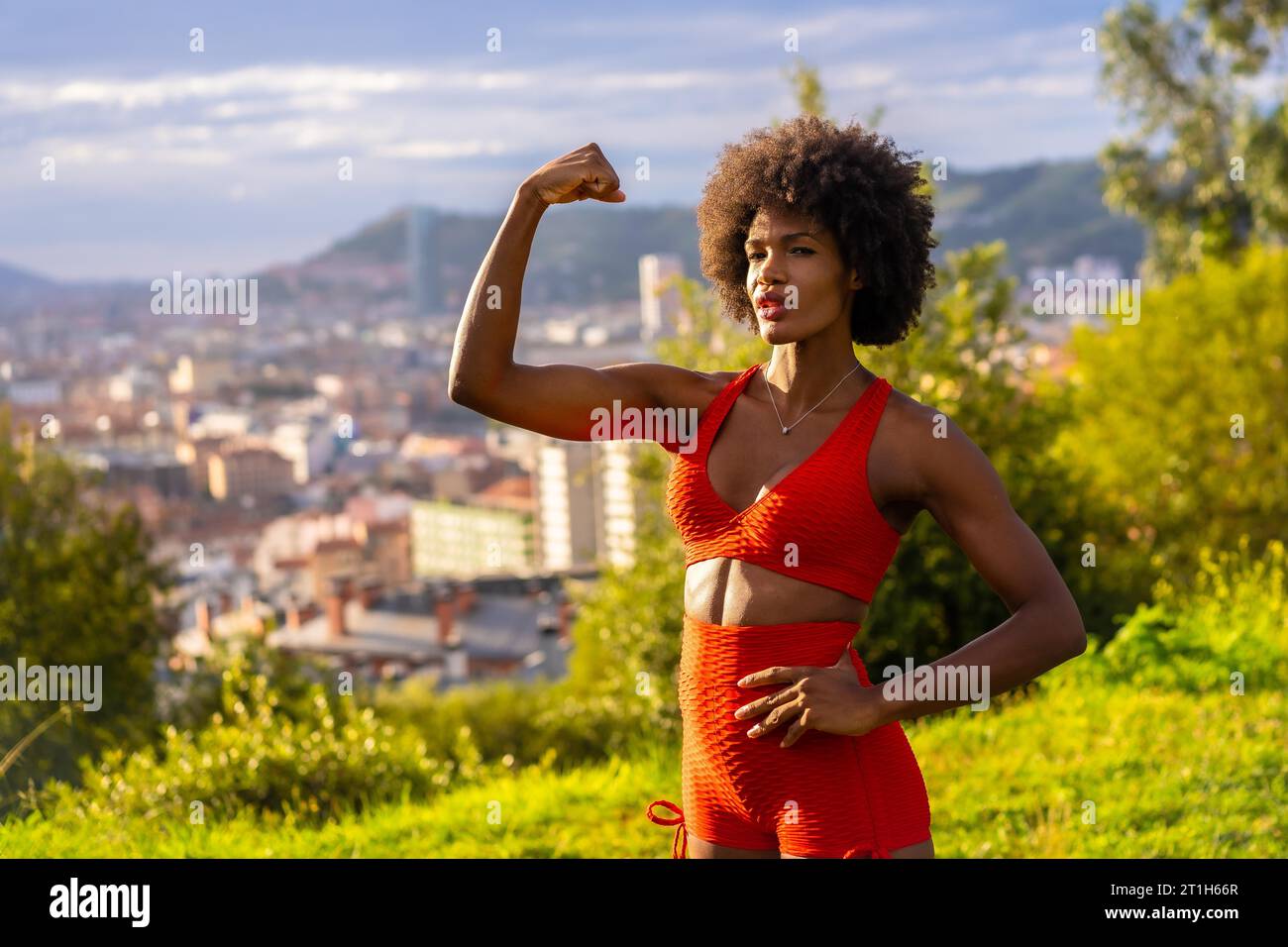 Fitness mit einem jungen schwarzen Mädchen mit Afro-Haar, zeigen Muskeln, Training auf dem Feld, rote Sportanzug, fit Mädchen, gesundes Leben, Kopierpaste Raum Stockfoto