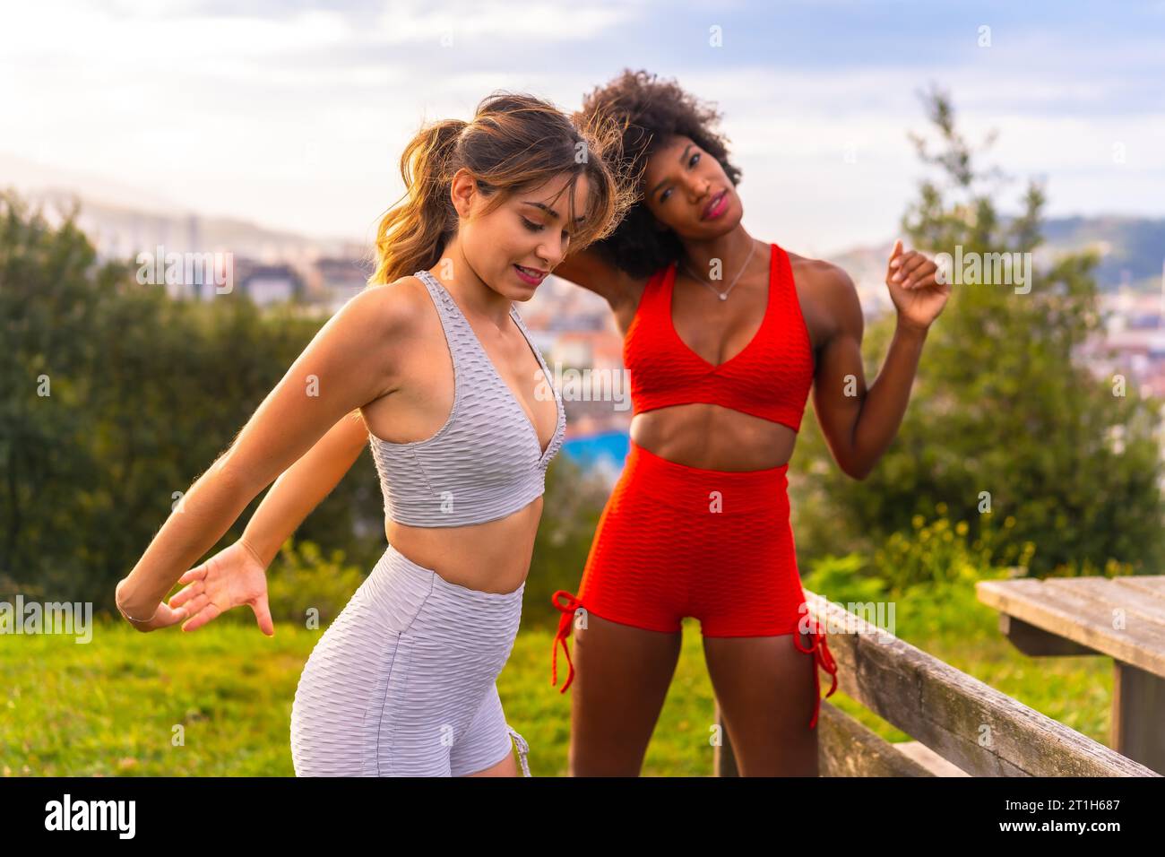 Weißes blondes Mädchen und dunkelhäutiges Mädchen mit Afro-Haar, das sich streckt, bevor es im Park Sport gibt. Gesundes Leben, Fitness, Fitness Mädchen Stockfoto