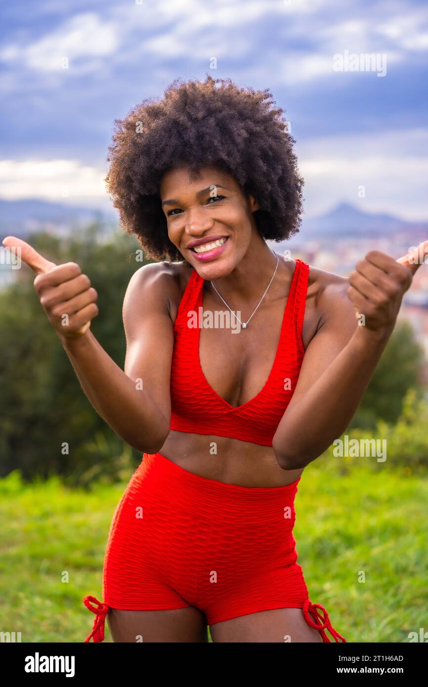 Fitness mit einem jungen schwarzen Mädchen mit Afro-Haaren, Übungen mit großer Freude machen, auf dem Feld trainieren, grauer Sportanzug, fittes Mädchen, gesundes Leben Stockfoto