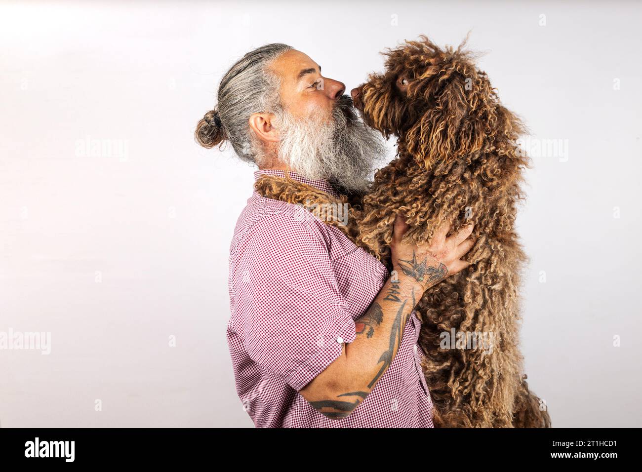 Ein bärtiger Mann küsst und umarmt seinen Wasserhund. Liebe zwischen Besitzer und Hund. Isoliert auf weißem Hintergrund. Studio-Porträt. Stockfoto