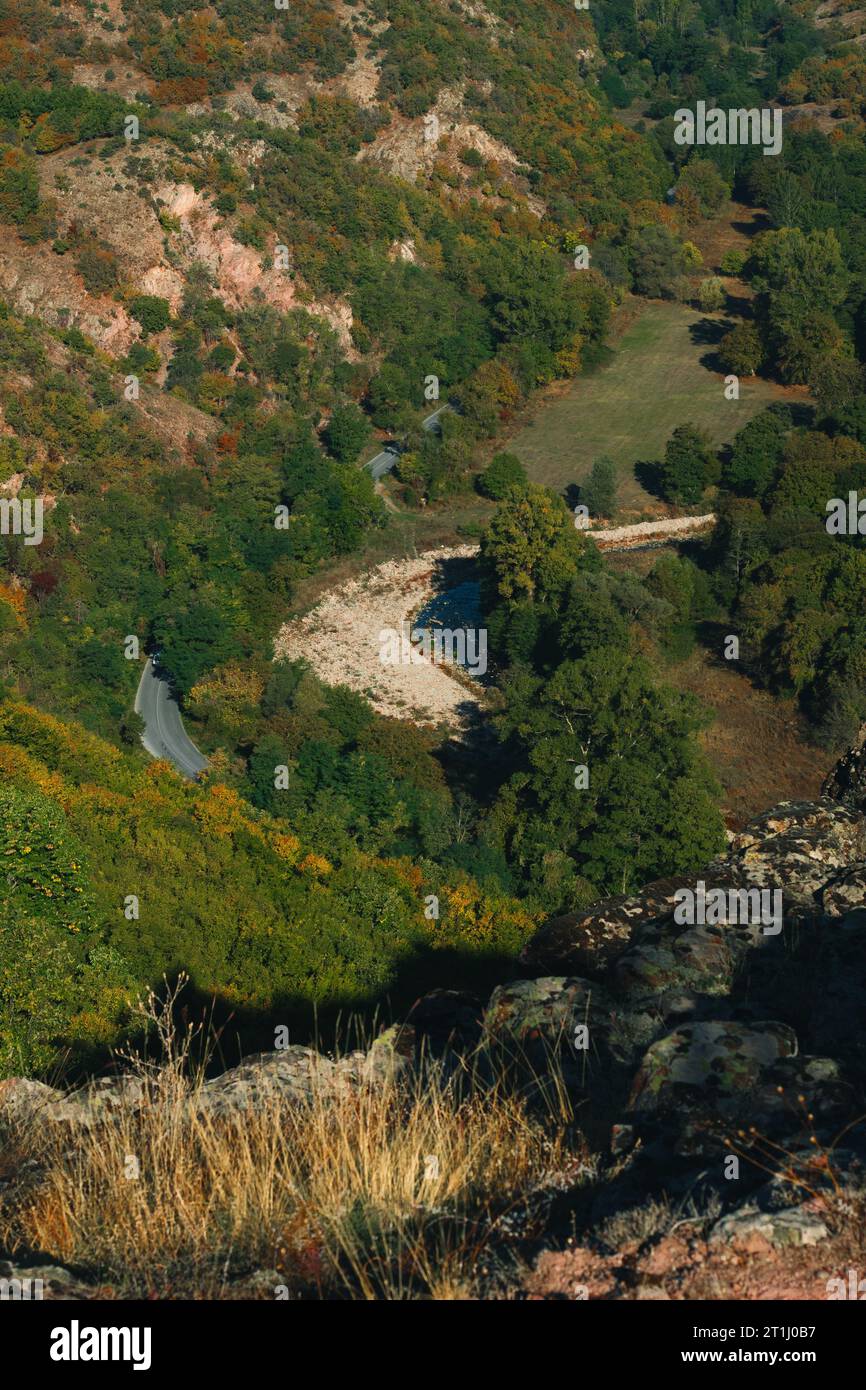 Eine Straße zwischen den Bäumen und dem Fluss neben der Straße in einem großen Canyon, aufgenommen von weitem mit Zoomobjektiv. Stockfoto