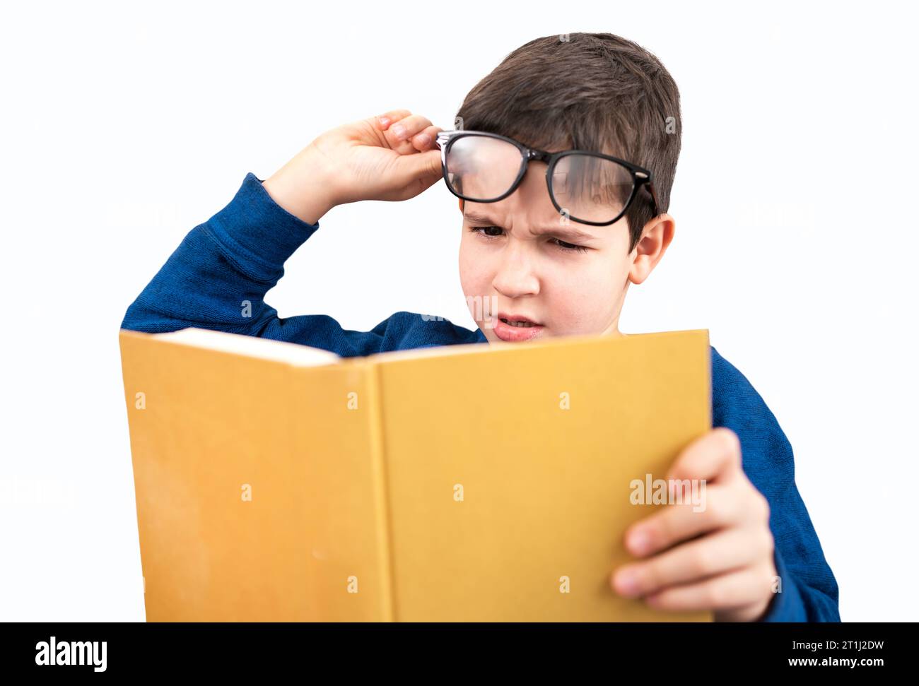 Ein Kind, das unter Augenbelastung leidet und zu Hause ein Buch lesen will Stockfoto