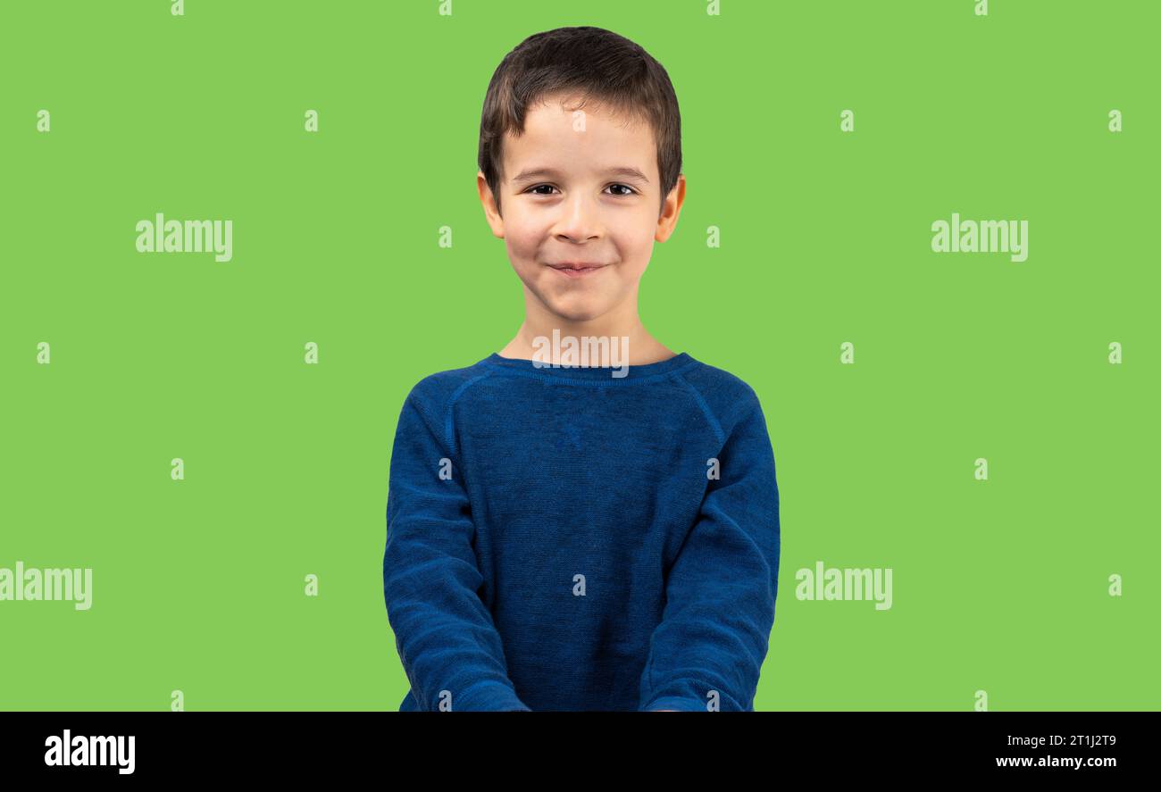 Dunkelhaariges kleines Kind mit lässigem T-Shirt, das auf isoliertem grünem Hintergrund mit einem fröhlichen und coolen Lächeln im Gesicht steht. Glückspilz Stockfoto