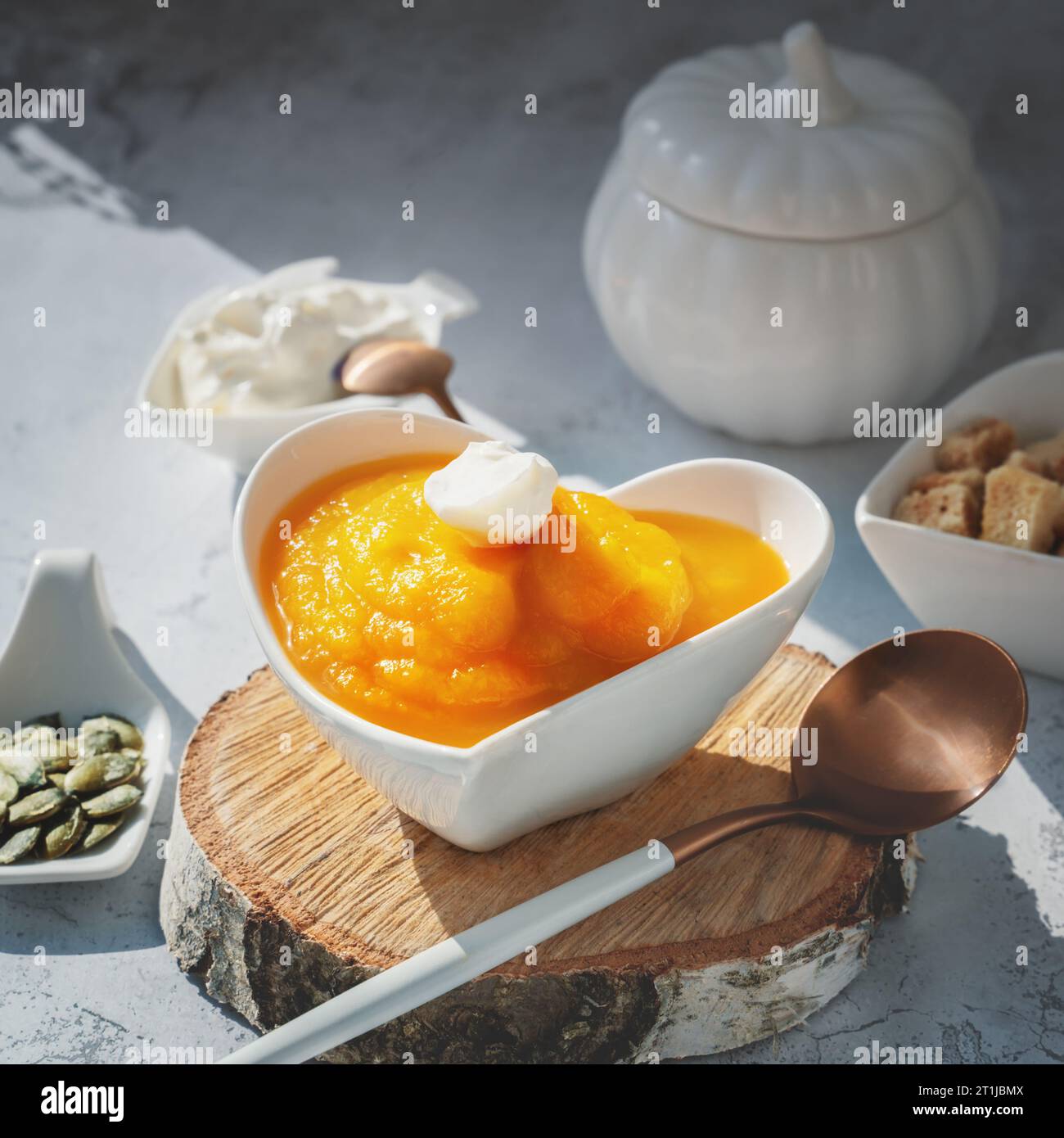 Kürbispüree Suppe mit Joghurt, Sesam und Kürbiskernen in einer herzförmigen Schüssel. Vegane Diät-Suppe für die ganze Saison. Stockfoto