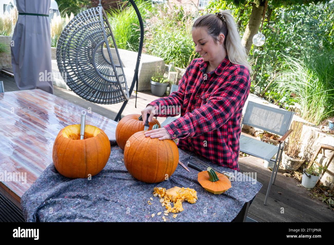 Blonde Frau, die die Spitze eines Kürbis öffnet, um halloween-Dekorationen mit einem Messer zu schnitzen Stockfoto