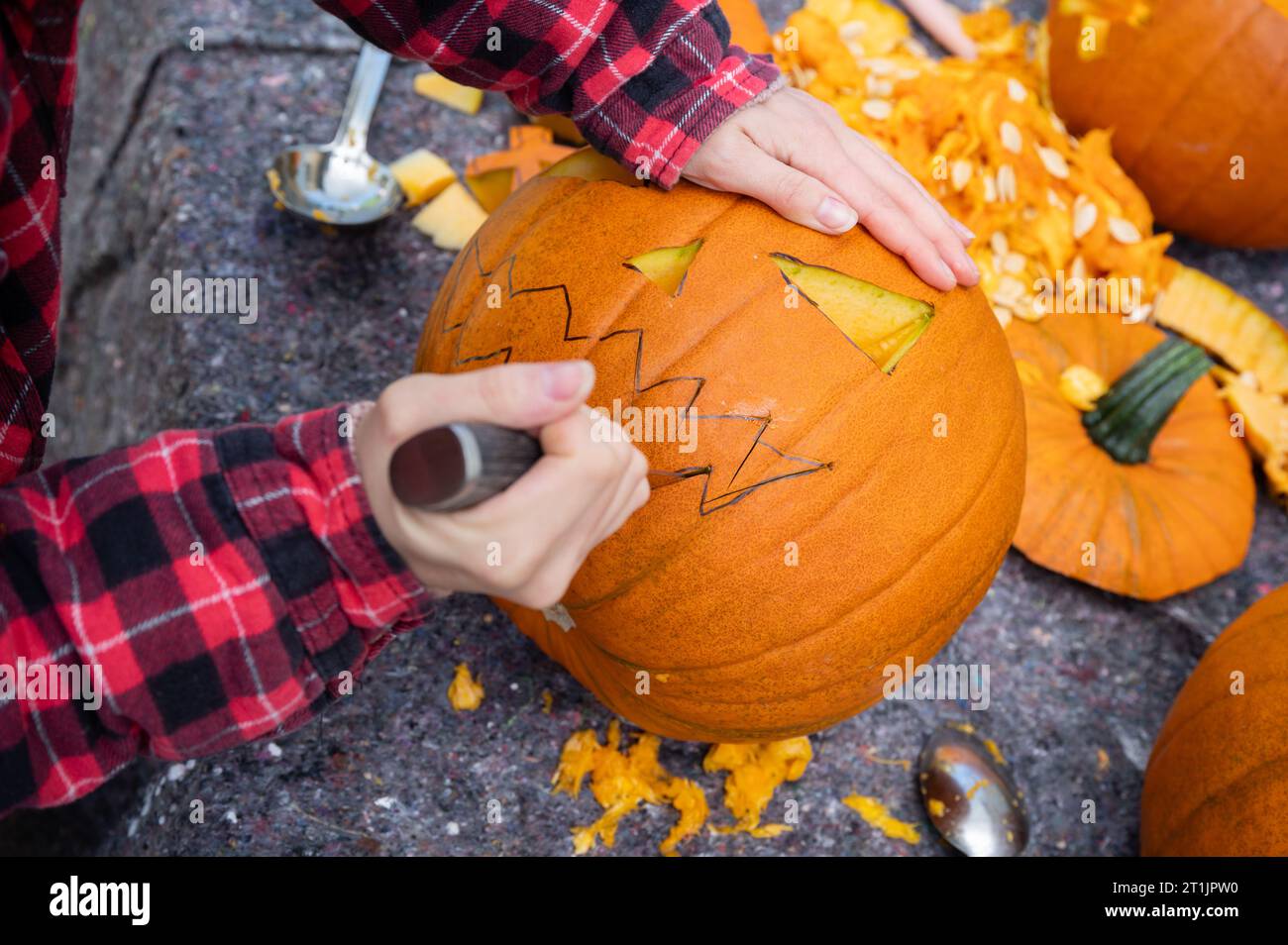 Zu Halloween wird ein Gesicht mit einem Messer in einen orangen Kürbis geschnitten Stockfoto