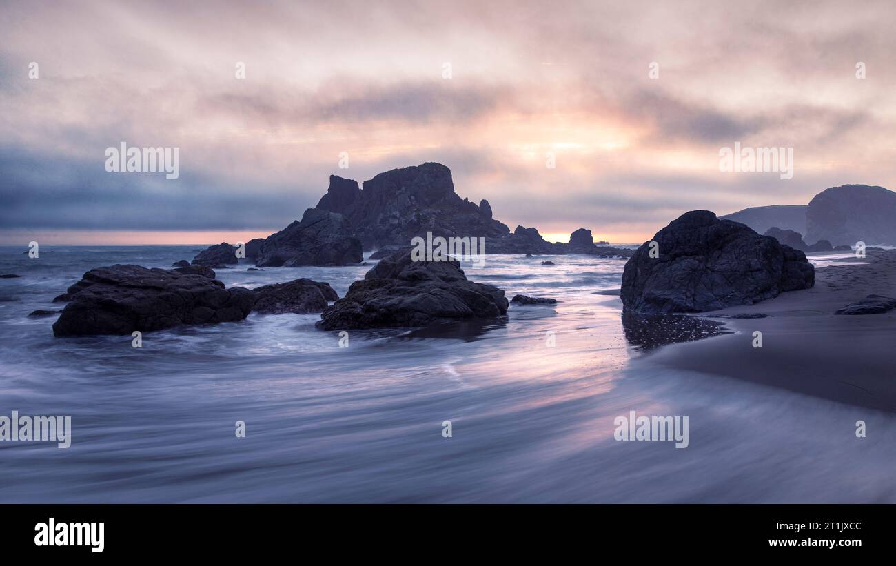 Sonnenuntergang am South Beach im Harris Beach State Park in Brookings, Oregon, mit Pastelltönen am Himmel, Felsbrocken und Meeresstapeln. Stockfoto