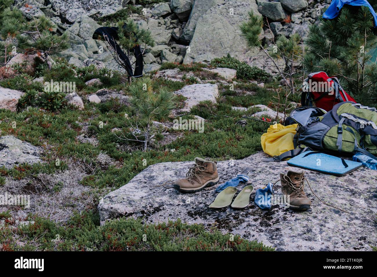 Trockenausrüstung nach einer Wanderung auf dem Campingplatz. Alte braune Trekkingschuhe, grüne Einlegesohlen und blaue Socken zum Trocknen nach dem Wandertag, auf Stein gelegt. W Stockfoto
