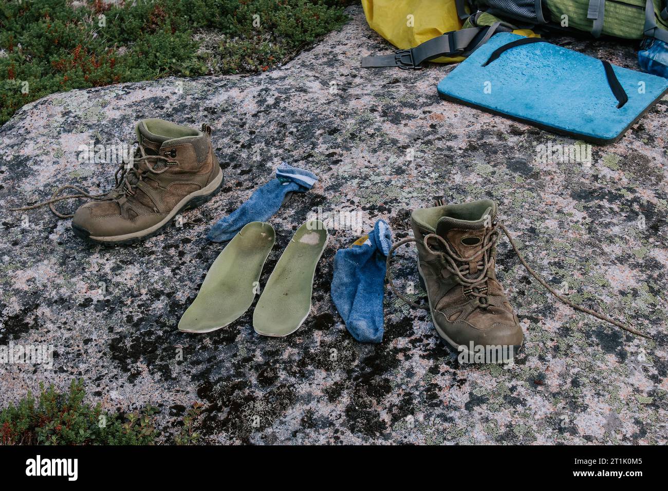 Alte braune Trekkingschuhe, grüne Einlegesohlen und blaue Socken zum Trocknen nach dem Wandertag, auf Stein gelegt. Nasse Füße während der Fahrt. Camping auf Reisen Stockfoto