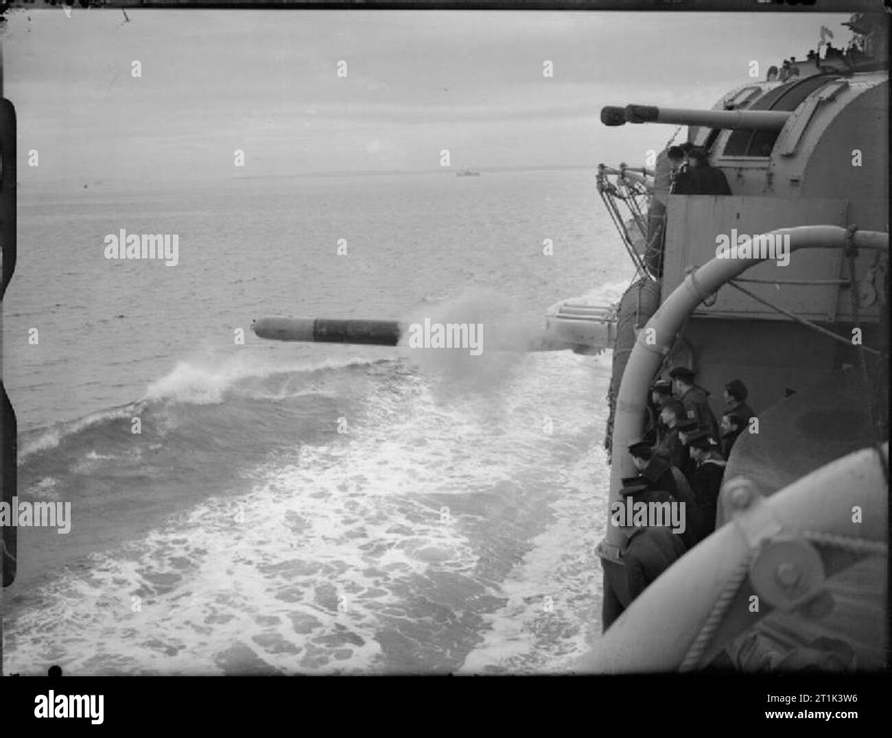 Die Royal Navy während des Zweiten Weltkriegs Mitglieder der Schiffsbesatzung mit einem Torpedo Verlassen der Torpedorohre mittschiffs beim Brennen Versuche an Bord der HMS SHROPSHIRE montiert. Eine der Twin 4cm Geschütztürme der Cruiser gesehen werden kann. Stockfoto