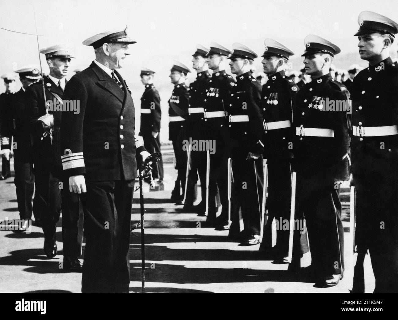 HMS Theseus in Korea. 18. März 1951, an Bord der Träger in Sasebo, Japan. Vice Admiral W G Andrewes, KBE, CB, DSO, Commander des Britischen Commonwealth und der Alliierten Flotte in der Koreanischen Gewässern, auch verantwortlich für die seeblockade von Korea, kontrolliert die Marine Guard an Bord der HMS THESEUS. Er ist durch Kapitän R S L Muldowney, RM, der Befehle der Marine Trennung im THESEUS, und der befehlshabende Offizier Captain S Schraube, DSC, RN begleitet. Die Marines sind von links nach rechts: HORNIST J Noyes, Windsor, Berks; Sgt J Geld, Deal, Kent; Marine G Leichtsinnige, Rochdale, Lancs; Cpl EINE R Mead, Budliegh, Stockfoto