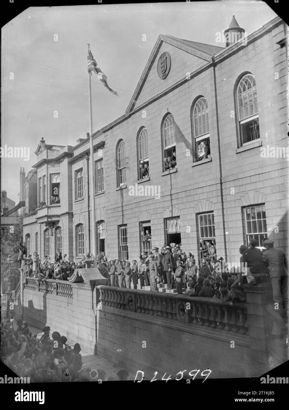 Channel Islands befreit - das Ende der deutschen Besatzung, Channel Islands, Großbritannien, 1945 Menschenmassen lächeln und winken als Leutnant E D Stoneman der britischen Task Force begrüsst die Anhebung der Union Flag in St Peter Port, Guernsey, nach der Unterzeichnung der Kapitulation Dokument. Dies ist das erste Mal, dass dieses Flag für fast fünf Jahre angehoben wurde. Stockfoto