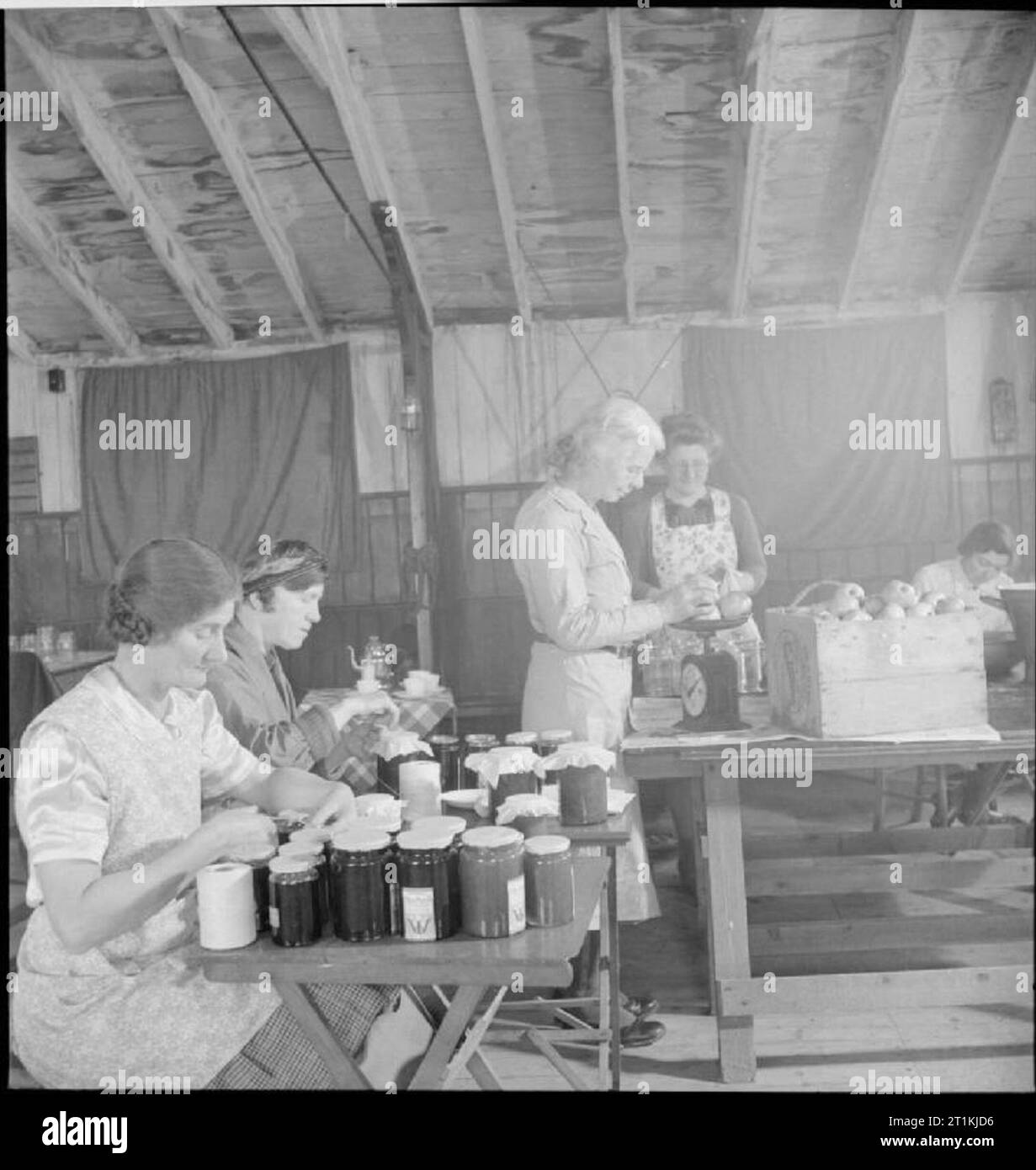 Gemeinschaft garten - Kriegszeit Nahrungsmittelproduktion auf Rowney Grün, Worcestershire, England, UK, 1943 die Mitglieder des Instituts schwer der Frauen bei der Arbeit, Stau im Frieden Hall (eine Armee Hütte in ein Dorf Halle umgewandelt) an Rowney Grün, Worcestershire. Die Beschriftung der Konfitüre-gläser im Vordergrund sind Frau Lee (links) und Frau Dodd. Wiegen die Frucht in der Mitte des Fotos ist Frau Nutting. Ein weiteres WI Mitglied kann hinter ihr gesehen werden, auch bei der Arbeit. Die Frucht wurde von den Leuten im Dorf, dem eigenen Garten, und der Zucker kam von der Regierung. Gemäß der ursprünglichen Caption, Th Stockfoto