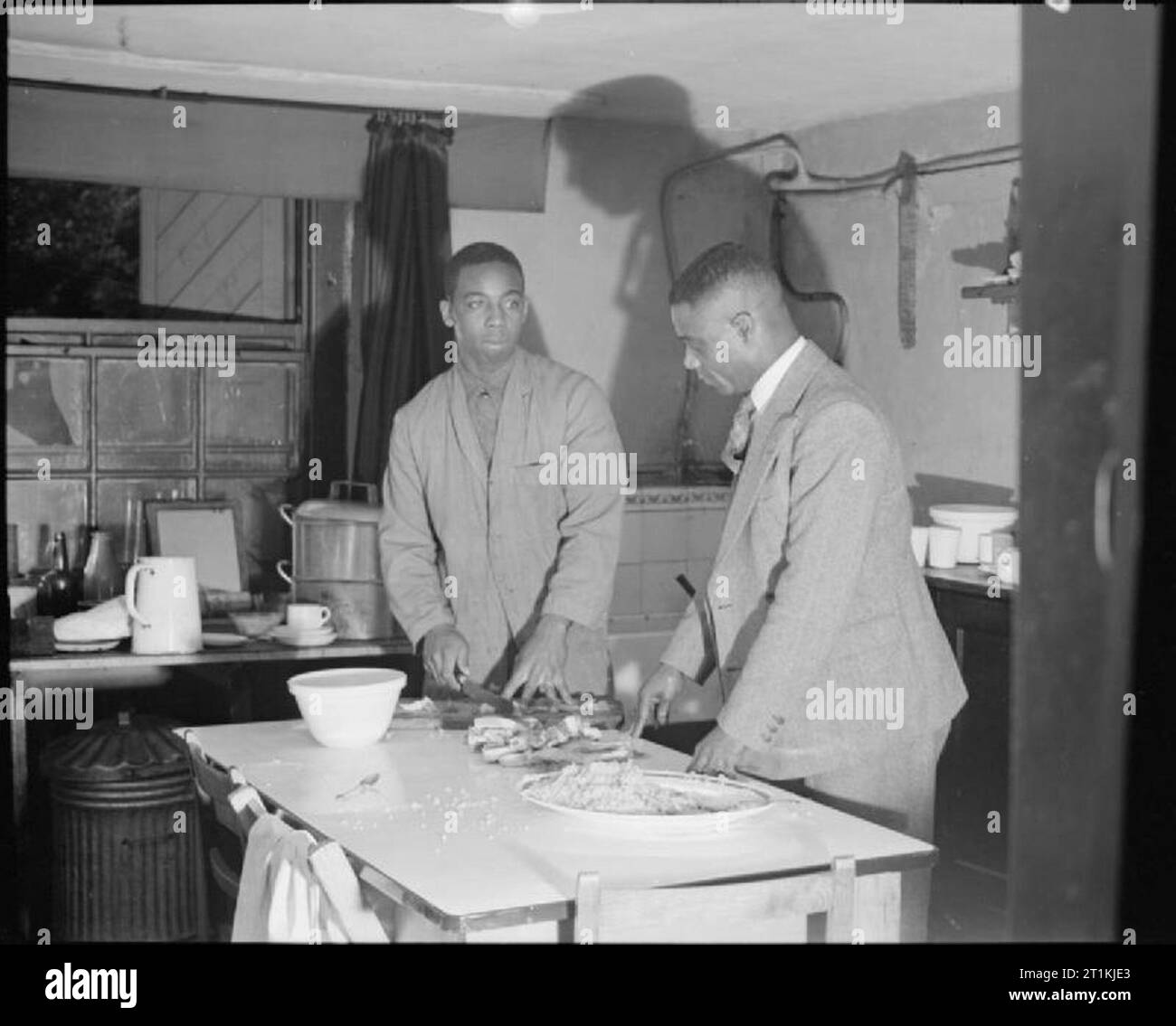 Colonial Rest Home-Empire Unterkünfte im Colonial House, North Shields, County Durham, 1942 Warden G U Minto (rechts) beobachtet, wie Gerald Vincent, allgemeine Faktotum, bereitet eine Mahlzeit in der Küche von Colonial House, North Shields. Gemäß der ursprünglichen Bildunterschriften, Minto hatte ein welterweight Boxing Champion wurde. Stockfoto