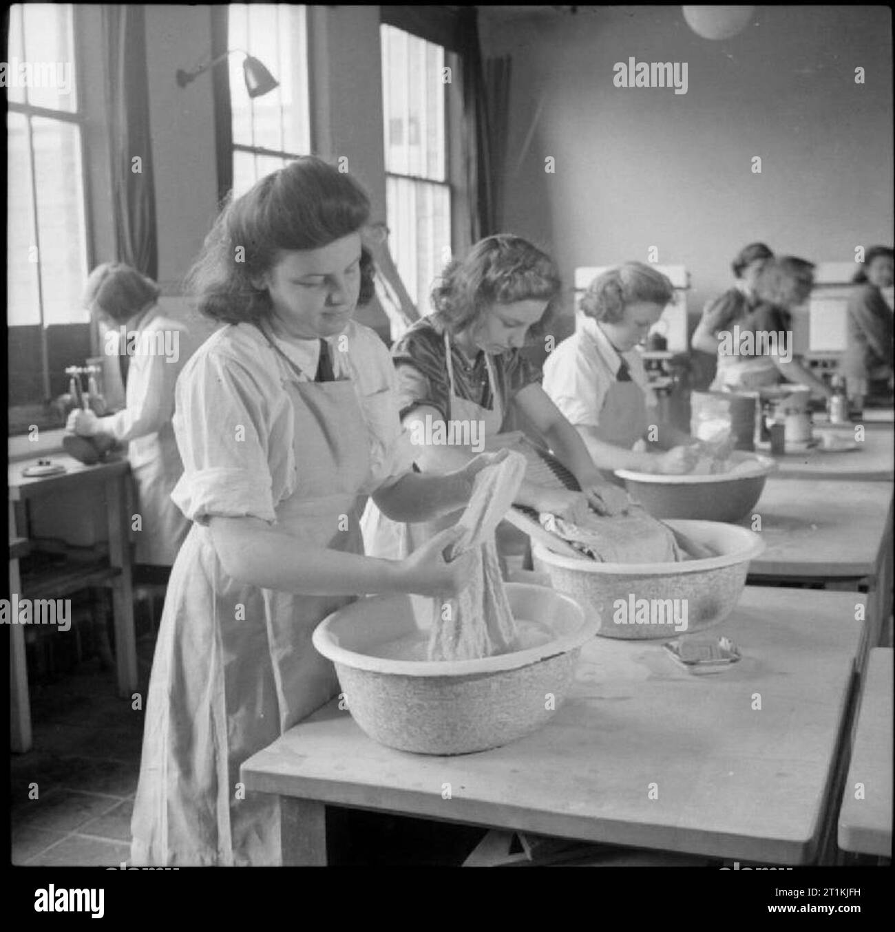 Land Schule - Alltag in Baldock County Council Schule, Baldock, Hertfordshire, England, UK, 1944 Mädchen an Baldock County Council Schule lernen Kleidung von Hand in einem Hauswirtschaft Klasse zu waschen. Sie sind mit Kunststoff Schalen mit Wasser auf den Tisch, und ein Mädchen (Mitte) wird mit einem waschbrett. Im Hintergrund, einer anderen Gruppe von Mädchen erhalten Unterricht in Kochen. Ein Mädchen an der Spüle auf der linken Seite des Fotos ist das Waschen bis der Topf Sie gerade verwendet hat. Stockfoto