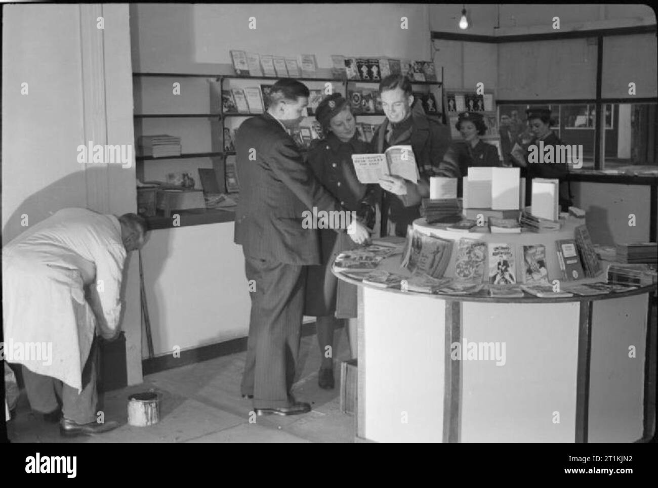 Ein Soldat Öffnet ein Shop-Trooper William Vaughan öffnet sich ein Buch Shop der Tottenham Court Road, London, England, UK, 1945 Herr William Vaughan zu einem Soldaten spricht und Mitglied des ATS, die ersten Kunden in seinen neu - Buch Shop der Tottenham Court Road, London eröffnet. Untersuchen Sie einen Schreibtisch Tagebuch jahr Buch für 1945. Im Hintergrund, mehrere andere ATS Frauen gesehen werden kann, das Browsen in den Regalen. In der linken unteren Ecke, ein Arbeiter ist den letzten Schliff an der Lackierung. Stockfoto