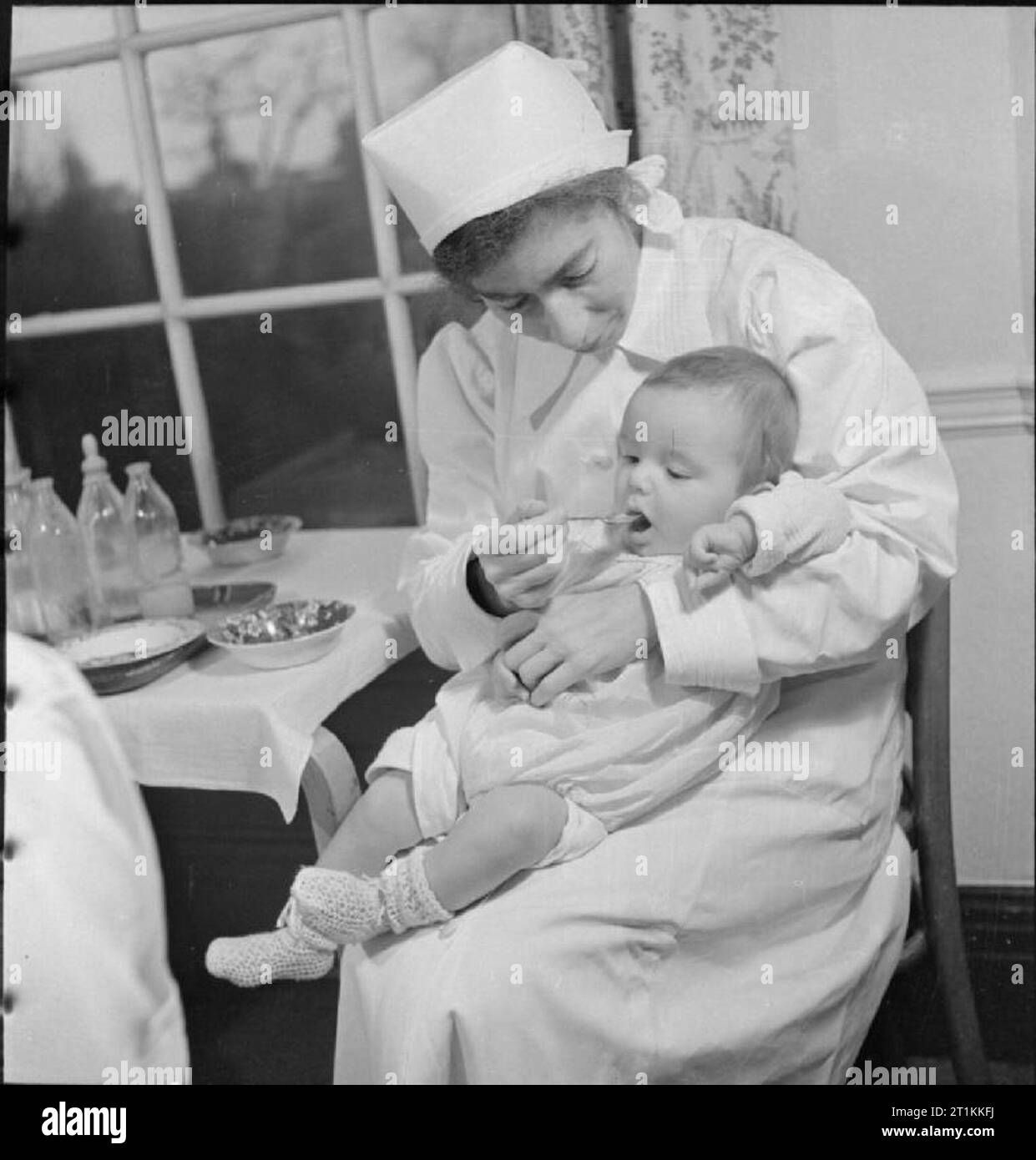 Pflegeeltern Plan London Baumschule - Pflege für vertriebene Kinder, London, England, 1941 8 Monate alten Teddy Hydd ist seine Ration von Orangensaft auf einem Löffel von einer Krankenschwester in der "Pflegeeltern Plan für Krieg Kinder Kindergarten in Hampstead zugeführt. Gemäß der ursprünglichen Legende:' Teddy, eine typische Krieg Baby, schliefen auf einer Plattform in Oxford Circus Station von 10 Tage ab. Ältester Bruder starb aus Tierheim Pneumonie. Angenehme Kind, aber die Anfälligkeit für alle Krankheiten ist aufgrund der Bedingungen in der frühen Kindheit". Stockfoto