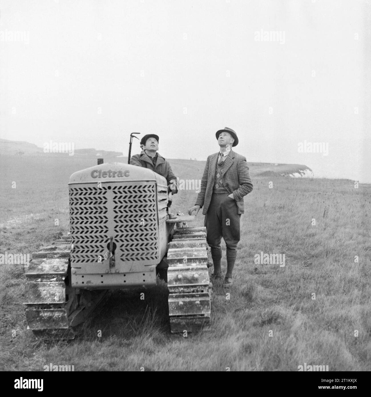 Front Bauernhof - Landwirtschaft auf die weißen Klippen von Dover, Kent, England, UK, c 1944 Bauer Gilbert Mitchell (rechts) Pausen in einem Chat mit seinem Traktor Fahrer Herr C Rogers, bei einem Flugzeug (nicht dargestellt), wie Sie in die Felder am Rand der weißen Klippen von Dover Arbeit zu suchen. Stockfoto