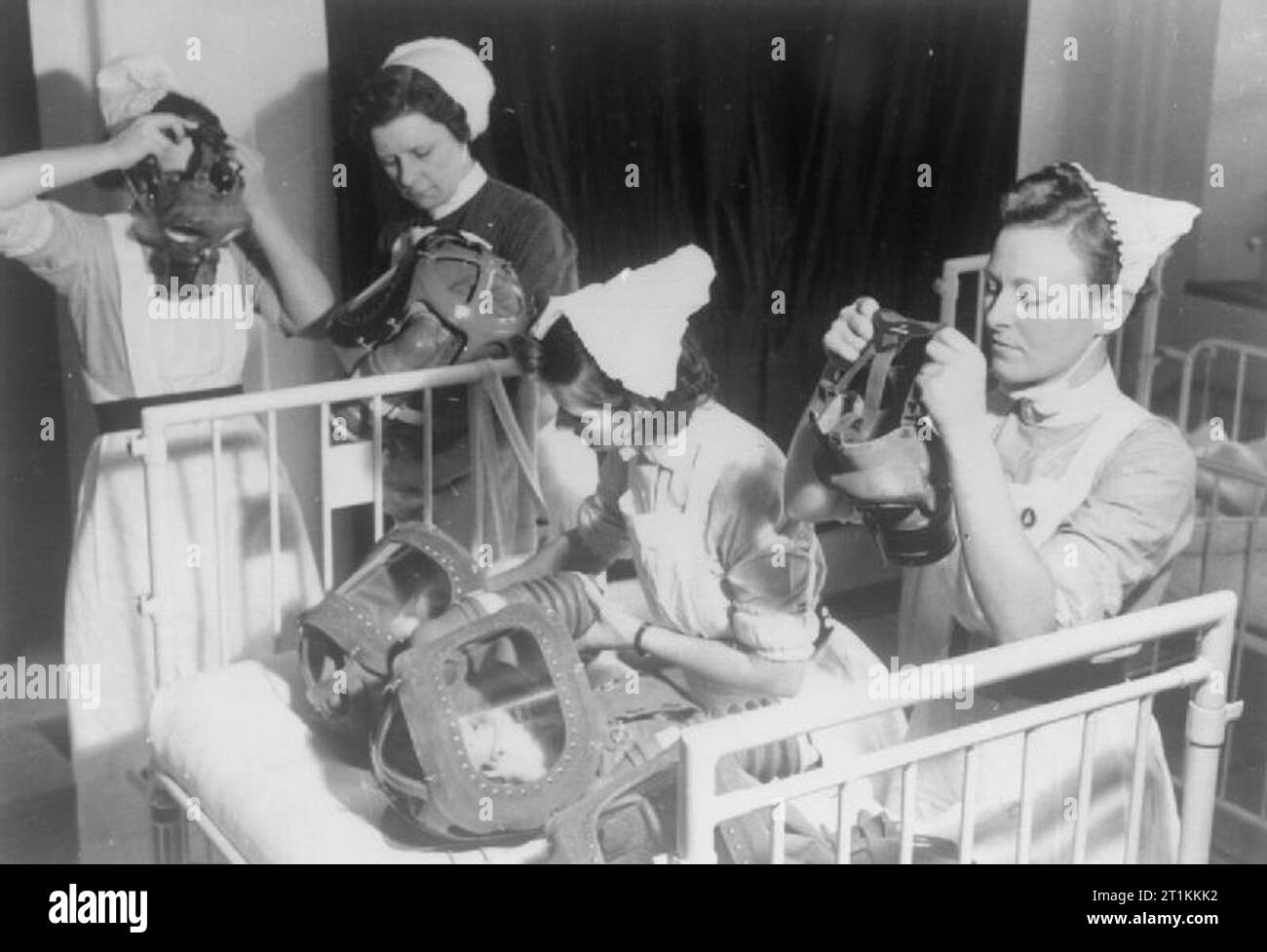 Gas Bohren in einem Londoner Krankenhaus - Gasmasken für Babys sind getestet, England, 1940 Drei Krankenschwestern ihre Gasmasken, während eine vierte Krankenschwester die Gasmasken von zwei Babys, die in der Wiege vor ihr besucht. Erwachsene wurden erklärt, um auf ihre eigenen Gasmaske vor dem Helfen, Kinder oder andere Erwachsene mit Ihnen zu setzen. Stockfoto