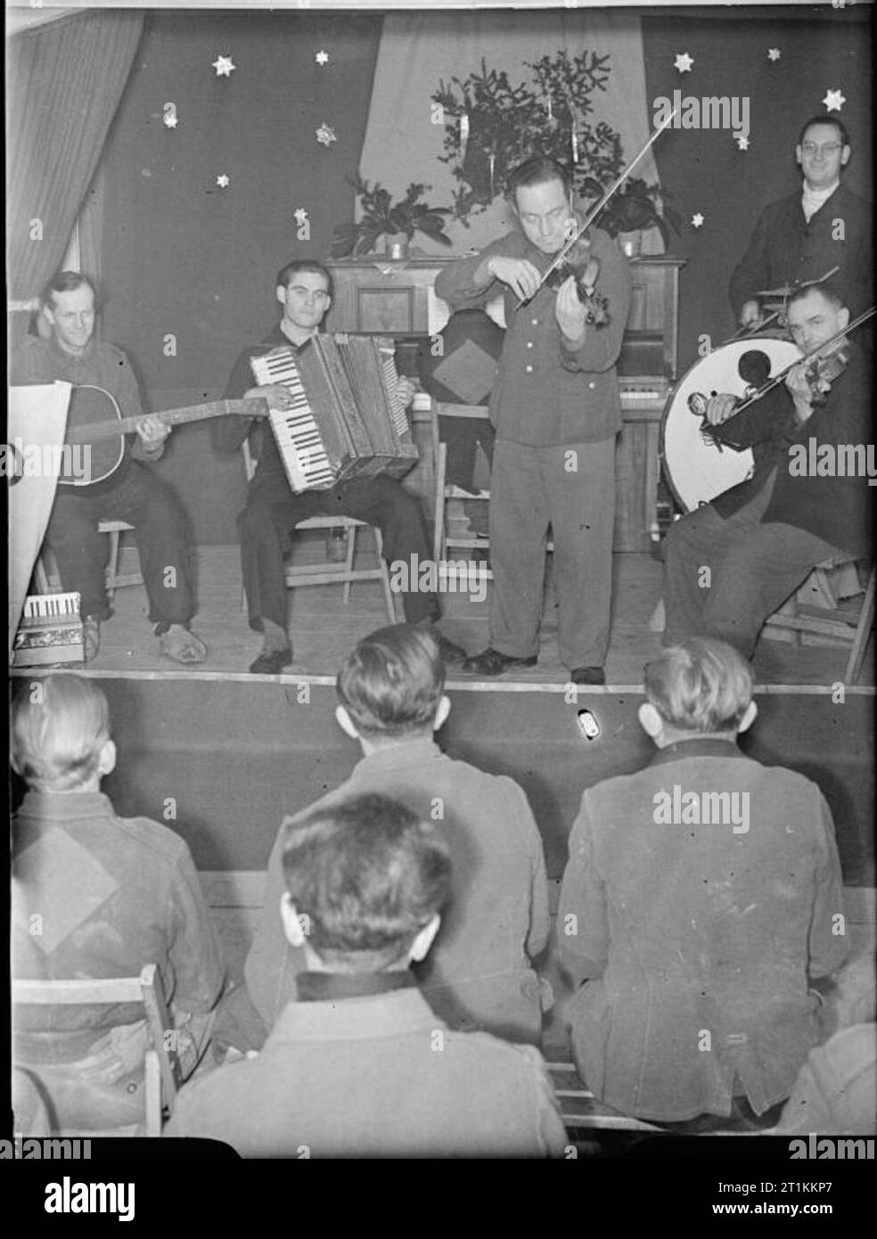 Deutsche Kriegsgefangene in Großbritannien - den Alltag in einem deutschen Kriegsgefangenenlager, UK, 1945 deutschen Kriegsgefangenen zu einem Konzert von einigen ihrer Mitgefangenen auf der Bühne in einem Kriegsgefangenenlager hören, irgendwo in Großbritannien. Instrumente: Gitarre, Akkordeon, Violine und Klavier. Der Hintergrund der Bühne ist mit Folie Sterne und das Klavier ist mit Tannenzweigen geschmückt, was darauf hinweist, dass es Weihnachten - Zeit eingerichtet. Stockfoto