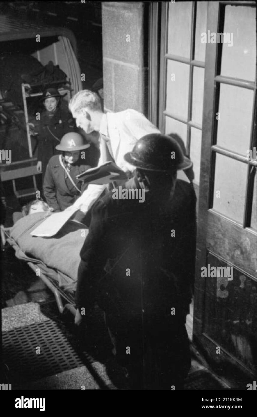 Guy's Hospital - Leben in einem Londoner Krankenhaus, England, 1941 Stretcher - Träger tragen einen Unfall in Guy's Hospital in London, als "Tally man' (eine Rolle, die normalerweise von einem Arzt gehalten) an der Tür wartet Anzahl jeder Unfall, wie sie in gebracht werden. Der tally Mann nimmt auch die Anzahl der Krankenwagen, der Unfall ins Krankenhaus gebracht. Stockfoto