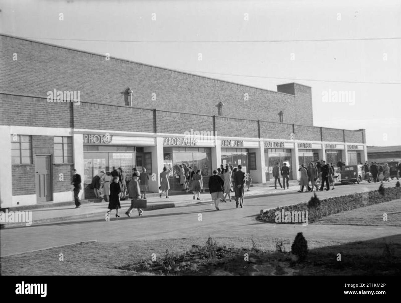 Holiday Camp wieder gehen - den Alltag bei einem Butlins Holiday Camp, Filey, Yorkshire, England, UK, 1945 Männer, Frauen und Kinder wandern vorbei an der Parade der Geschäfte in Butlin's Holiday Camp, Filey. Von Links nach Rechts, die Beschriftungen über den Geschäften sind: Fotos, Sportswear, Schuhputzmaschine/-service, Post, Kiosk, Kostüme und Radio Butlins. Die Legende besagt, dass jedes Butlin's Camp ist eine komplett eigenständige Urlaub Stadt und Filey" hat sogar einen eigenen Bahnhof, ein Teil der LNER'. Die Schuhputzmaschine/-service ist ein wichtiges Geschäft, denn, so der ursprüngliche Titel' jede Woche einen Preis von einer Woche' Stockfoto
