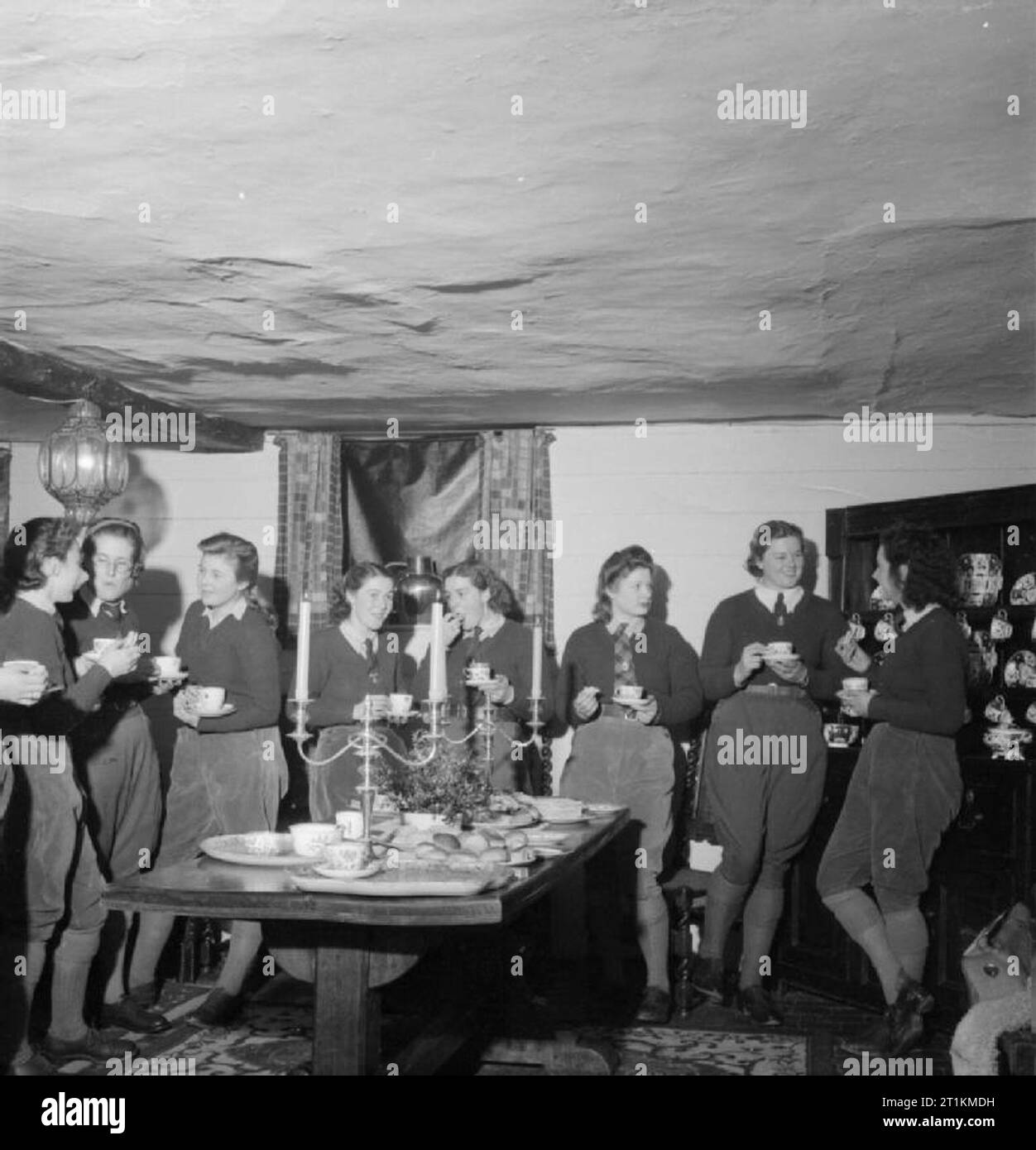 Landgirl's Day - den Alltag und die Landwirtschaft in West Sussex, England, UK, 1944 29 Jahre alte Land Mädchen Rosalind Cox (zweite Form rechts) und ihre Kollegen Kaffee, Sandwiches und genießen in der Kerze chat beleuchteten Innenraum des 400 Jahre alten Prattendens Cottage in Bury, West Sussex. Die Hütte war von der radio star Mabel Constanduros vor dem Krieg belegt. Diese Zusammenkünfte jeden Montag Abend und geben dem Land Mädchen die Möglichkeit, sich zu entspannen und miteinander reden. Stockfoto