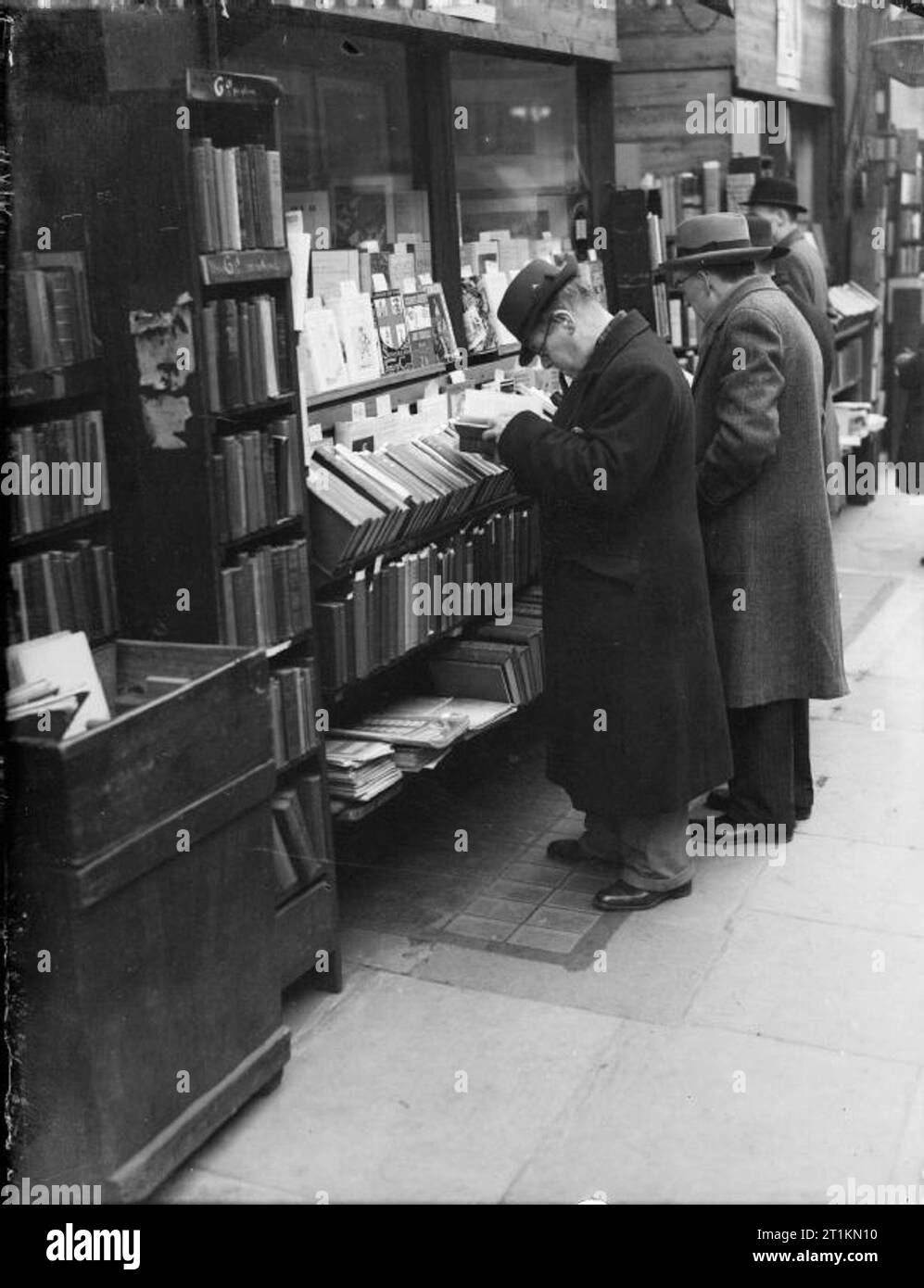 London im Frühjahr 1941 - Alltag in London, England zwei Männer lesen Bücher auf dem Display außerhalb dieses Bookshop, irgendwo in London. Die bücherregale Linie der Gehsteig vor dem Geschäft, so dass Passanten zu durchsuchen, bevor Sie kaufen. Stockfoto