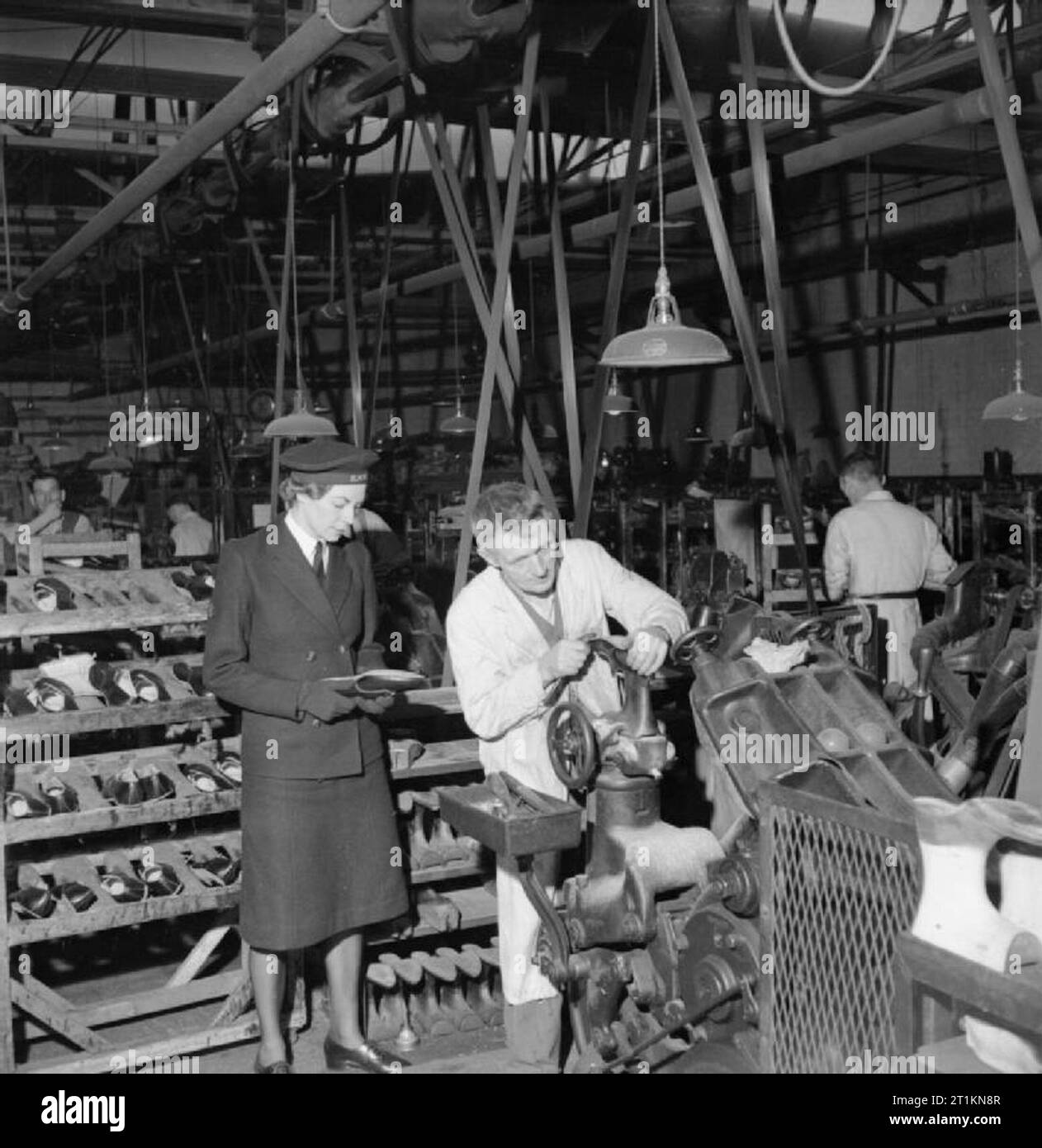 Herstellung von Schuhen für die zaunkönige - die Herstellung von Schuhen für die Women's Royal Naval Service bei einer Fabrik in den Midlands, England, Großbritannien, 1944 Mitglied der Royal Naval der Frauen Service Uhren ein Schuster bei der Arbeit in einer Fabrik, die irgendwo in den Midlands. Die Legende besagt, dass dieser Teil des Fertigungsprozesses ist als "untere Nivellierung', wobei verschiedene Schichten von Nähten und viel Druck benötigt werden, für die alleinige Wissen. Hinter der Zaunkönig, einen Stapel des Wartens Schuhe ist deutlich sichtbar. Im Hintergrund, verschiedenen anderen Männer können bei der Arbeit auf den Faktor gesehen werden. Stockfoto