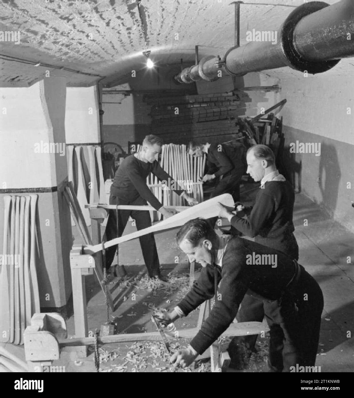 National Fire Service auf Krieg - Krieg Arbeit in einer Feuerwache, London, England, UK, 1943 Feuerwehrleute der NFS auf einer Feuerwache der Themse Bildung machen Paddel für Angriff Profil für die Admiralität. Die Paddel ankommen Rund - aus einer Fabrik, und die Feuerwehrleute müssen Sie Beenden von Hand geformt. In der Nähe von Kamera zu Kamera am weitesten, sie sind: Feuerwehrmann G R De Vere, Feuerwehrmann P E Prestidge, Feuerwehrmann H S Bellingham (wer ging in die Fabrik, um den Prozess zu lernen und anschließend unterrichtete seine Kollegen) und Feuerwehrmann H W E Upjohn. Stockfoto