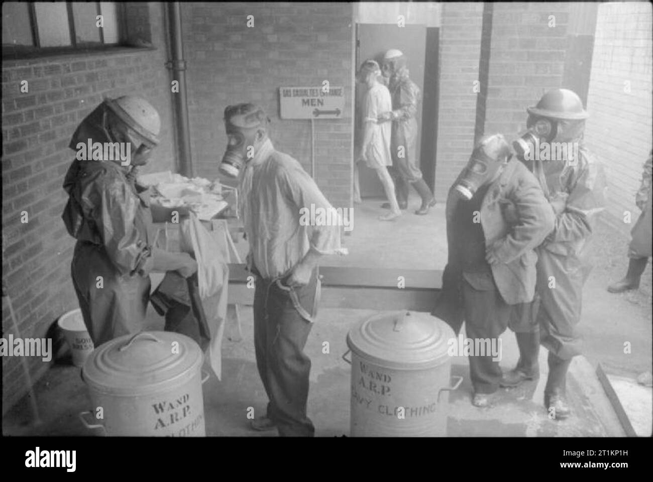 Air Raid Vorsichtsmaßnahmen auf dem britischen Home Front - die Arbeit der Gas Reinigung Center, Wandsworth, London, England, 1941 Zivilschutz Arbeiter in volle anti-gas Schutzanzüge, stahlhelme und Gasmasken assist gas Opfer bei der Ankunft in diesem Gas Reinigung Zentrum in Wandsworth, London. Die Opfer müssen ihre äußere Kleidung entfernen und in die spezielle Fächer im Vordergrund sichtbar, bevor er in die nächste Phase der Sanierung begleitet wird. Ihre Kleider werden ein separates Dekontamination unterziehen. Das Schild im Hintergrund liest: "Gas Opfer Eingang Männer": Stockfoto