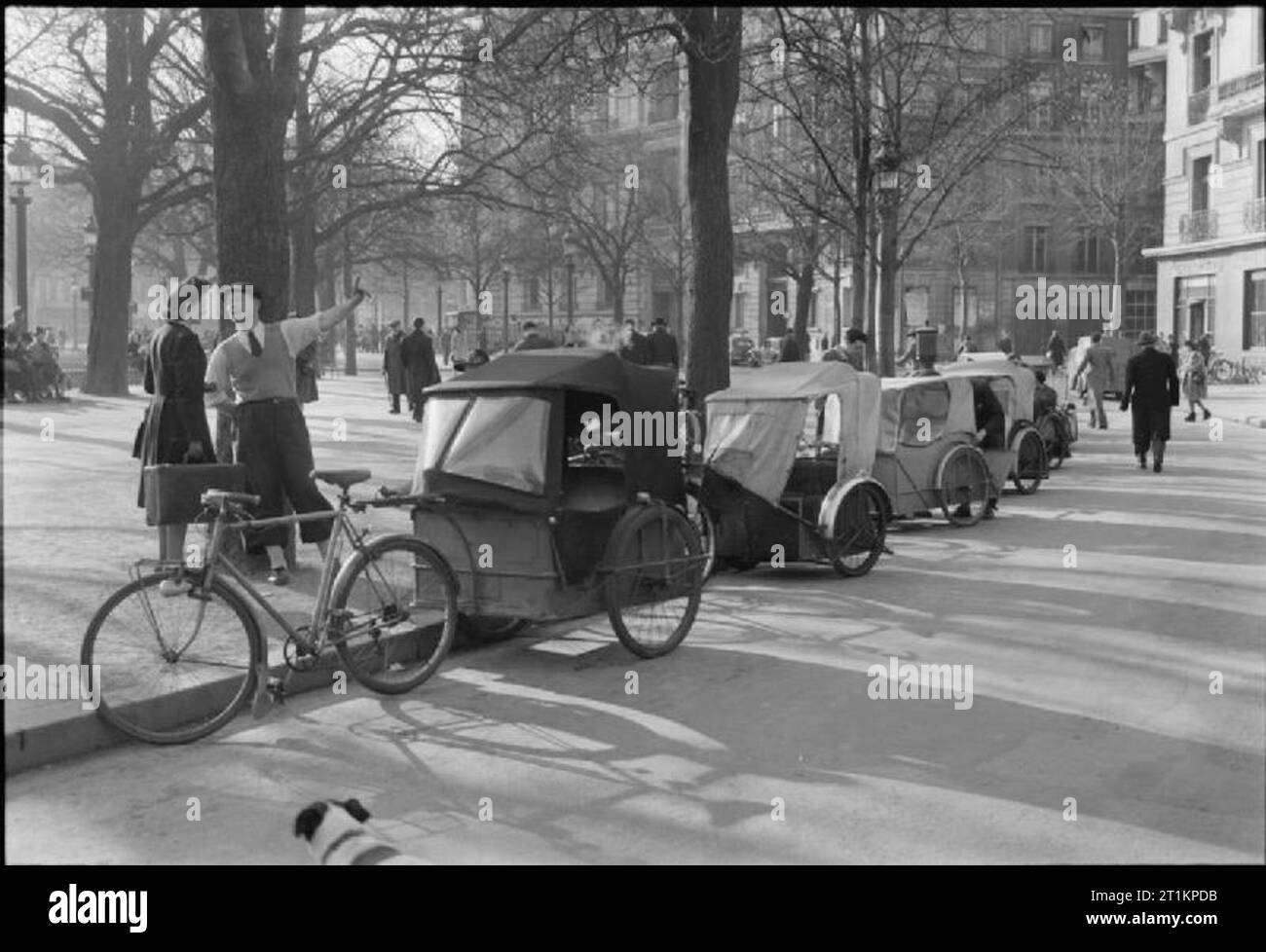 Paris, Spring 1945 - Alltag in Paris, Frankreich, 1945 eine allgemeine Ansicht eines cab Rang: Französischer Stil! Eine Reihe von Velo Taxis linie die aufkantung an einer baumbestandenen Straße in der Frühlingssonne, irgendwo in Paris. Fußgänger können klar gesehen werden, über ihr tägliches Geschäft gehen. Stockfoto